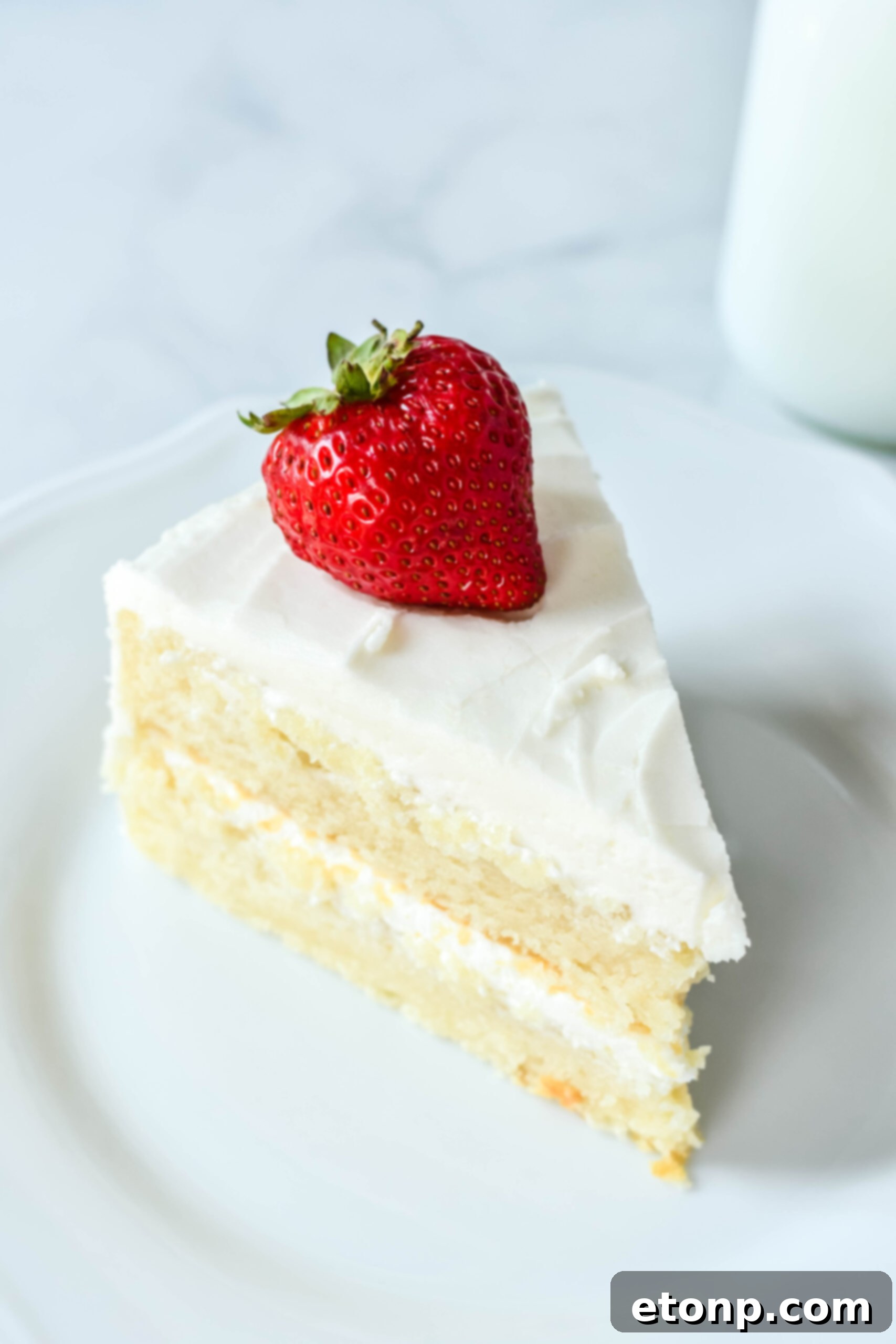 Up close view of a slice of Classic Vanilla Cake on a white plate garnished with a strawberry, highlighting its delicious layers.