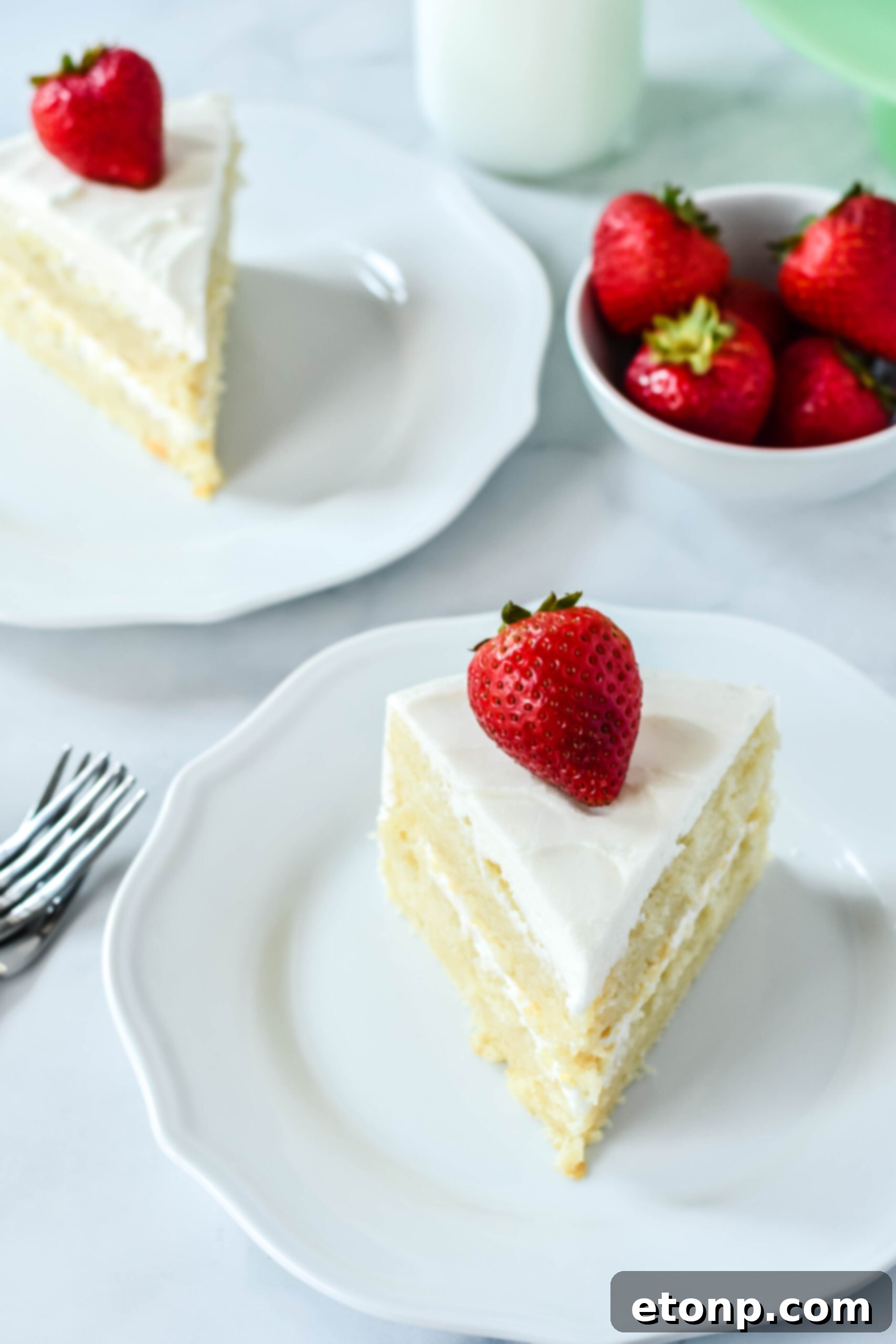 Front view of a slice of Classic Vanilla Cake on a white plate garnished with a strawberry, showcasing its inviting appearance.