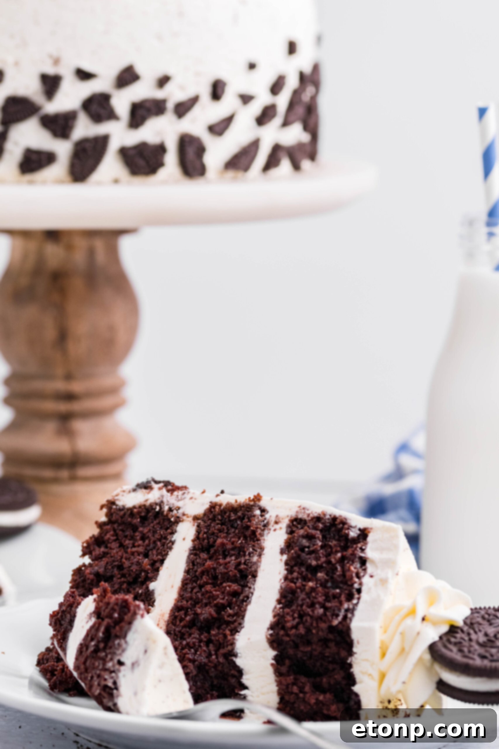 Front view of a slice of Double Stuffed Oreo Cake served on a white plate with a bite removed from a silver fork.