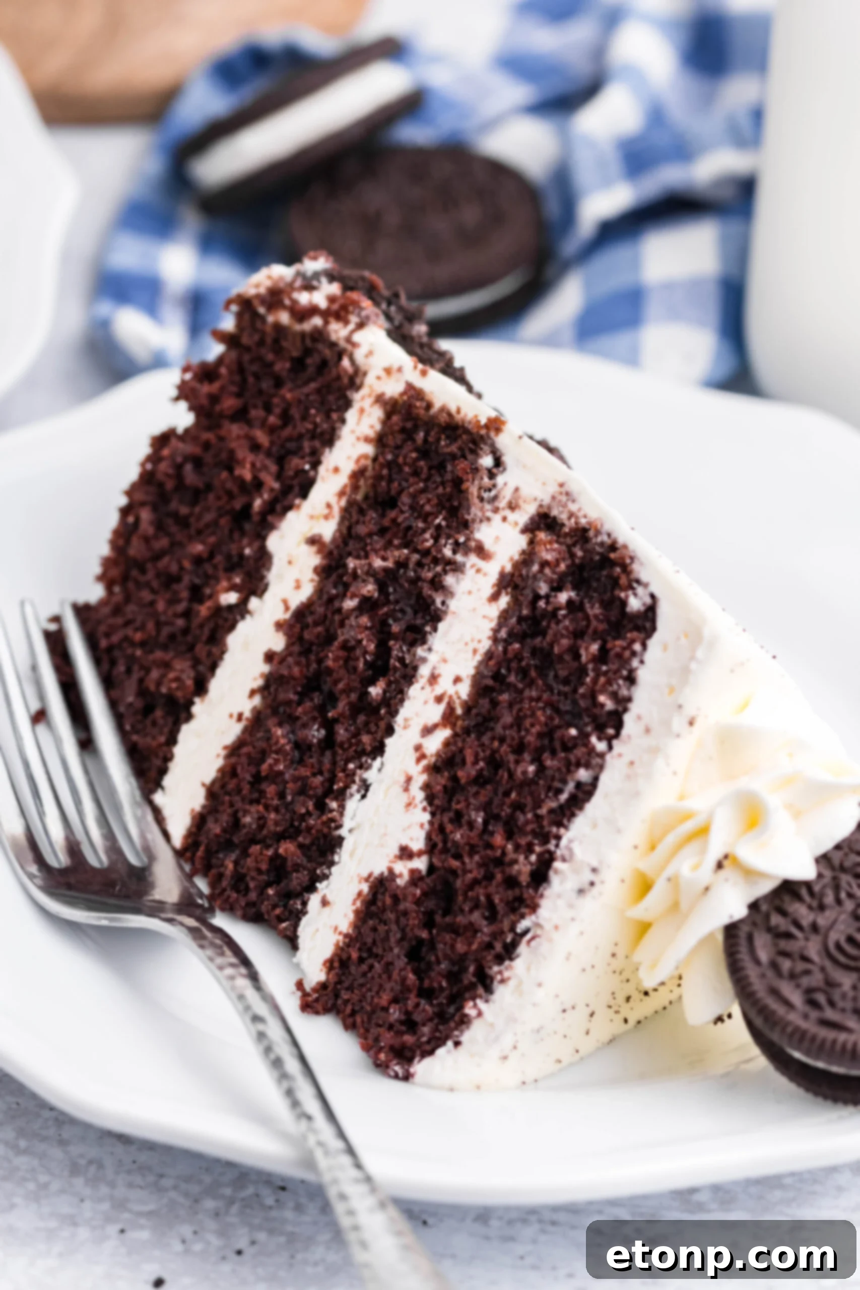 Front view of a slice of Double Stuffed Oreo Cake served on a white plate with a silver fork.
