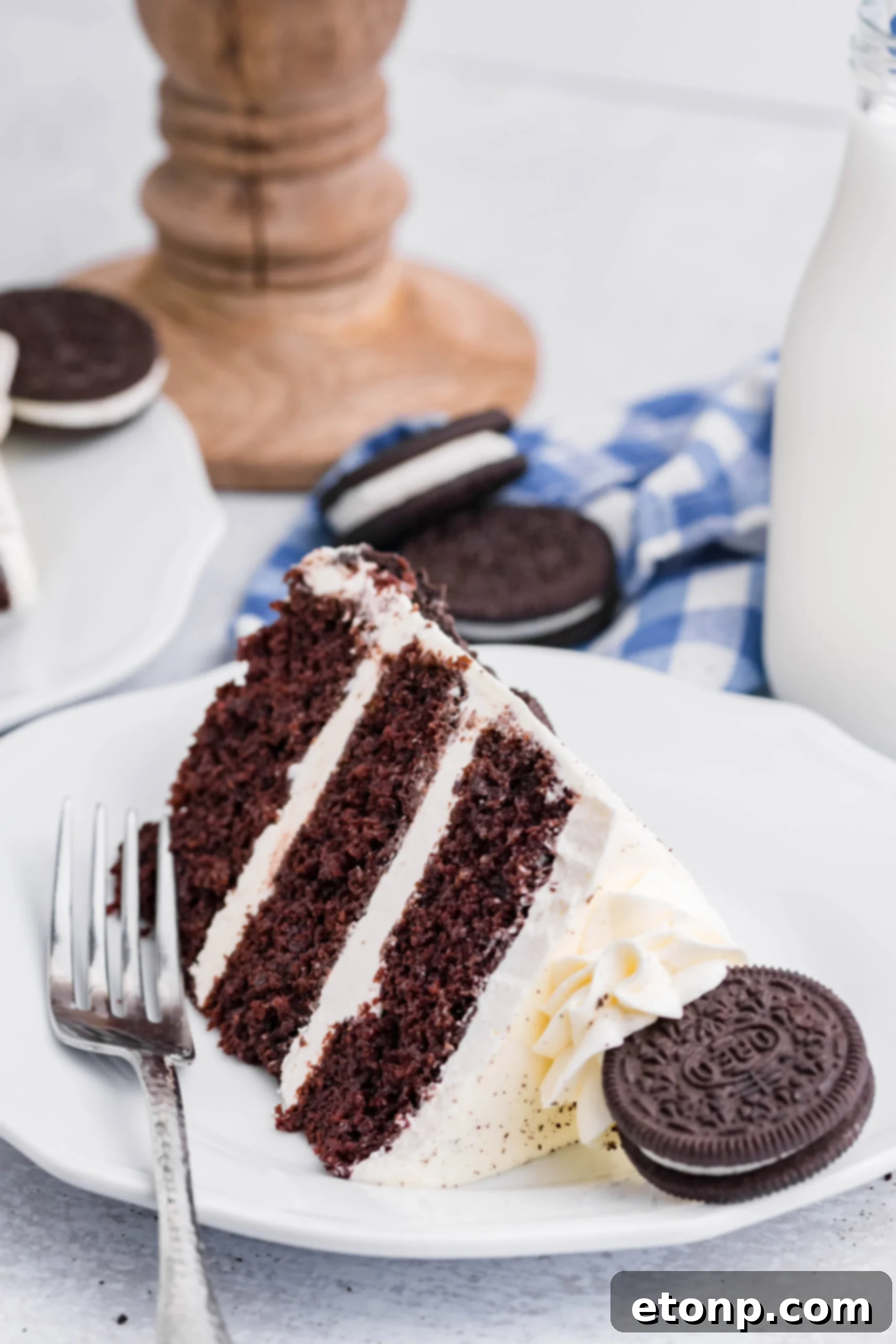 Front view of a slice of Double Stuffed Oreo Cake served on a white plate with a silver fork.