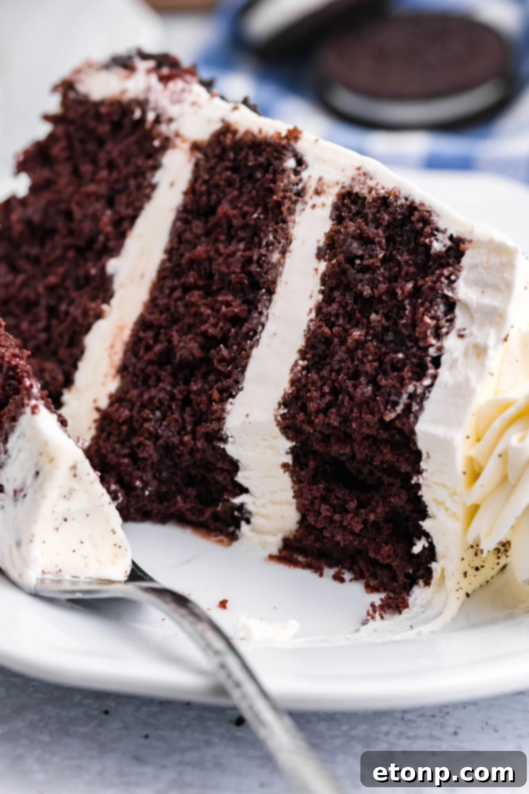 Close up view of a slice of Double Stuffed Oreo Cake served on a white plate with a bite removed from a silver fork.