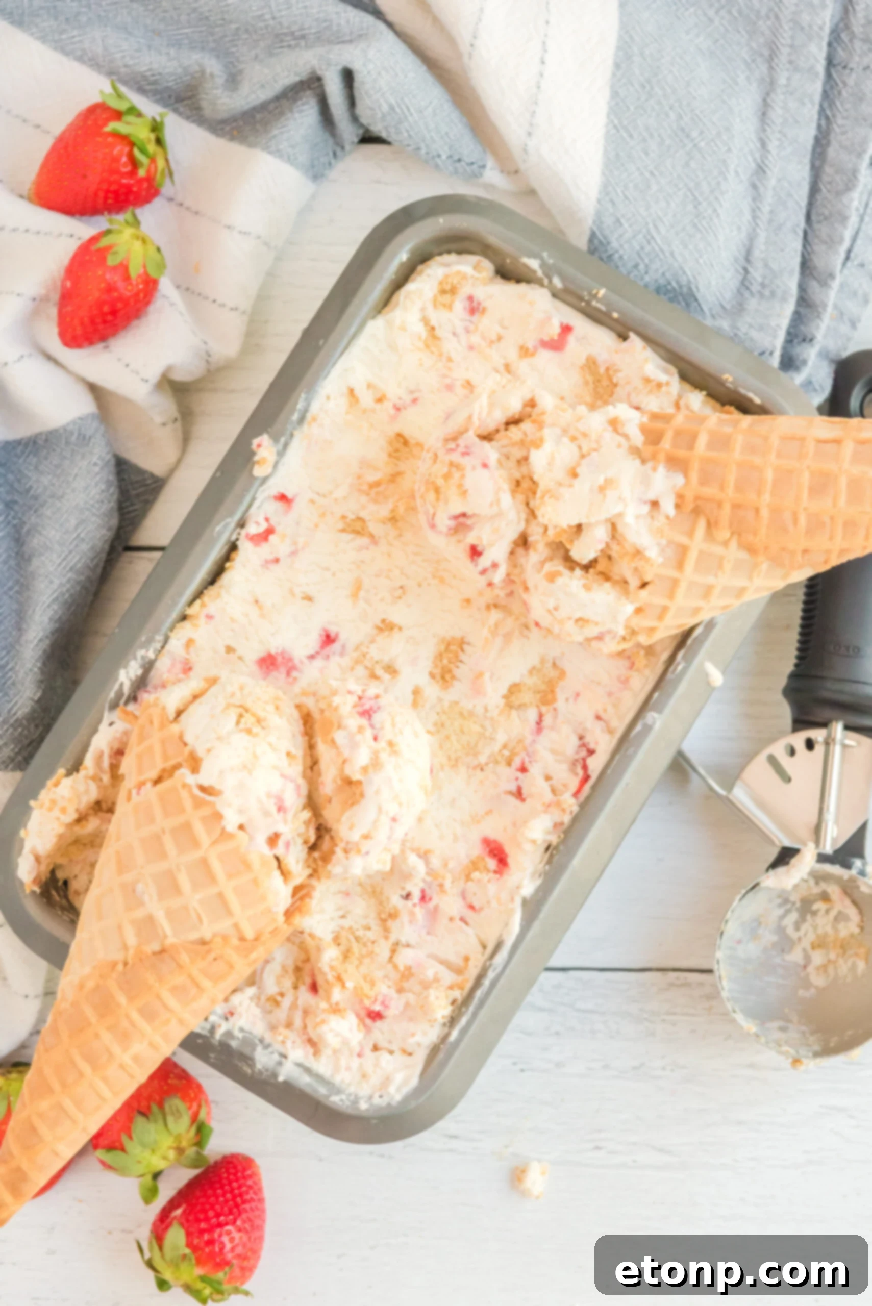 Overhead view of a pan full of Strawberry Cheesecake Ice Cream with two waffle cones laying on top.