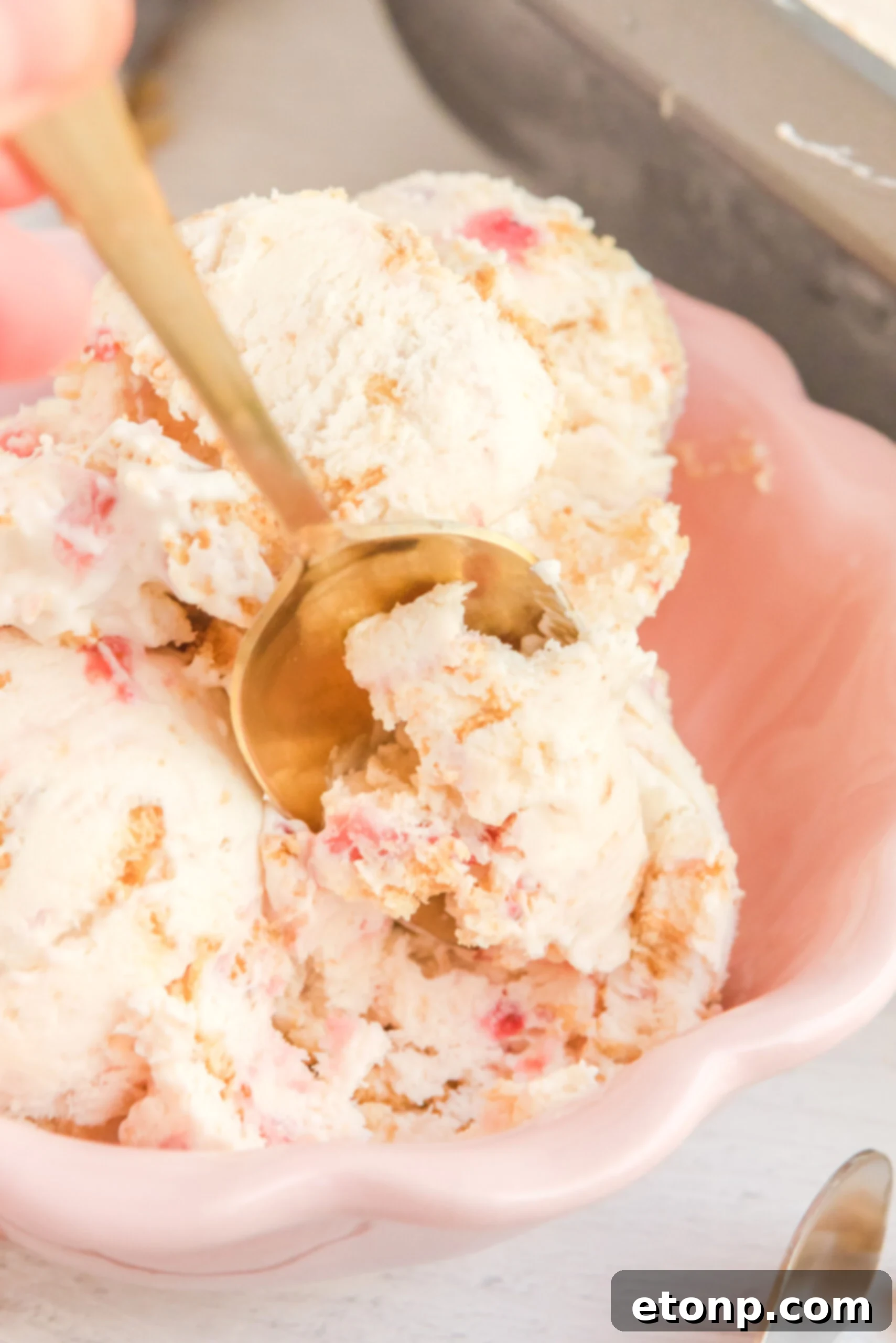 Close up view of a gold spoon removing a bite of Strawberry Cheesecake Ice Cream.