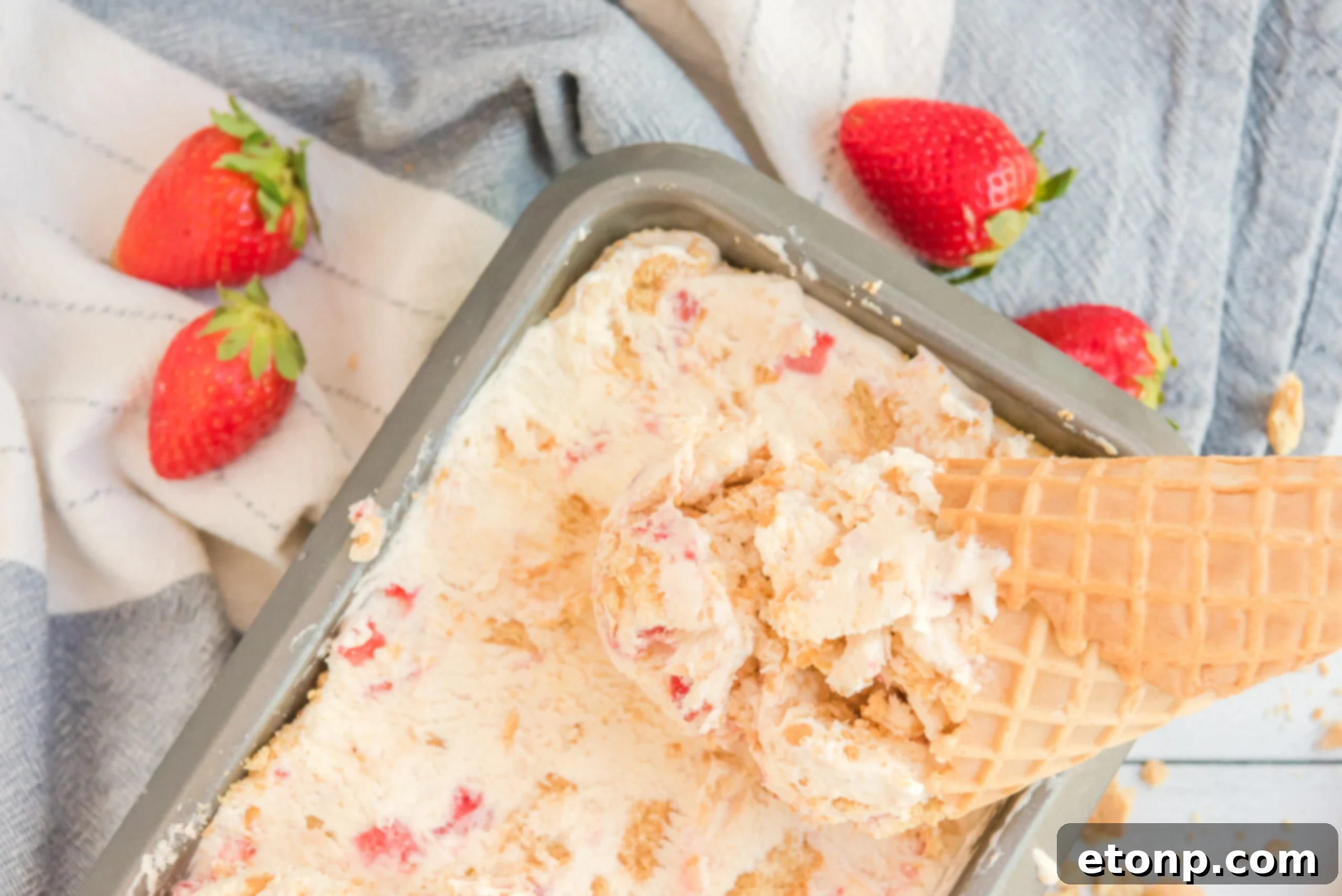Strawberry Cheesecake Ice Cream with a cone dipping in it.