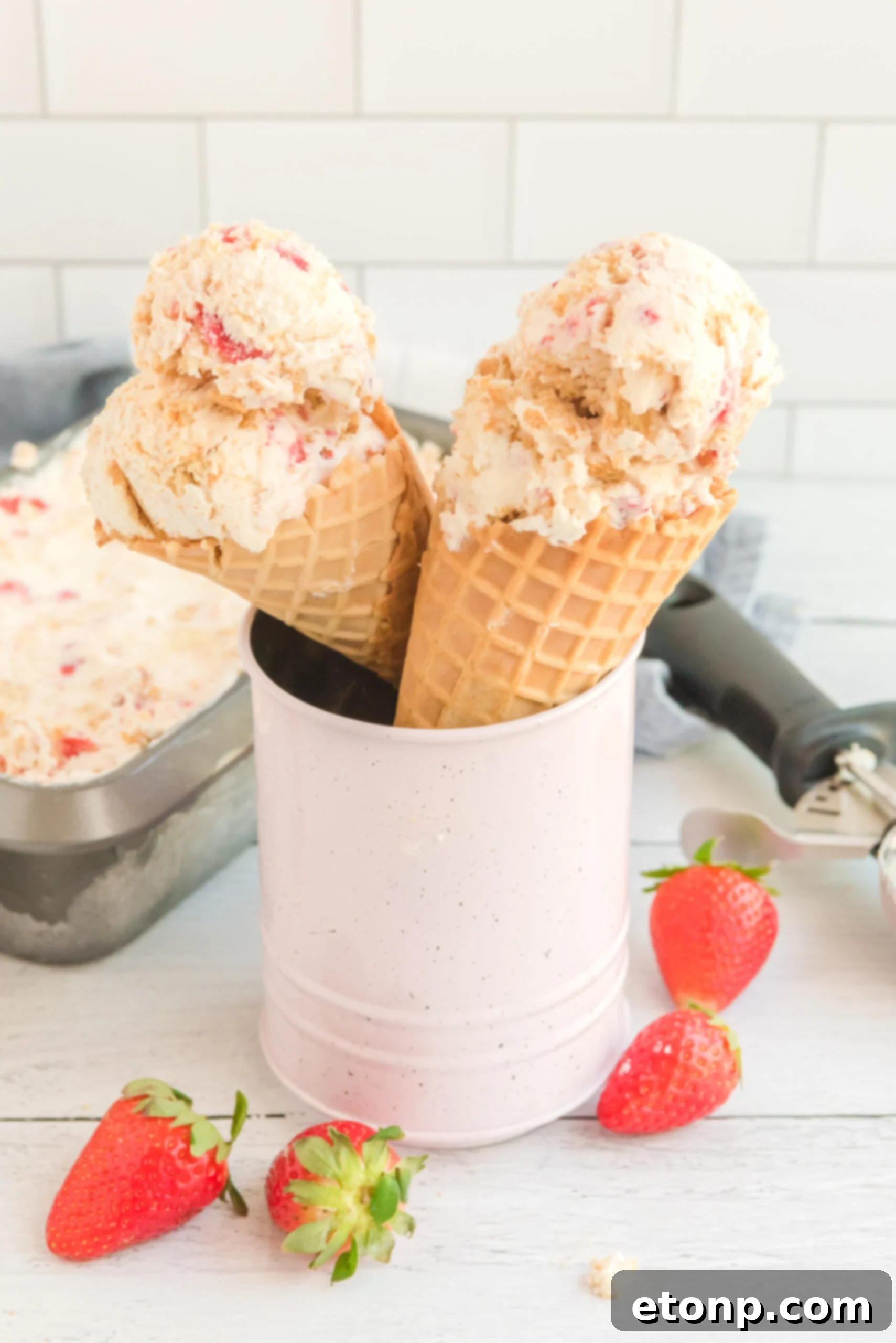 Front view of two waffle cones with a scoop of Strawberry Cheesecake Ice Cream in each cone.