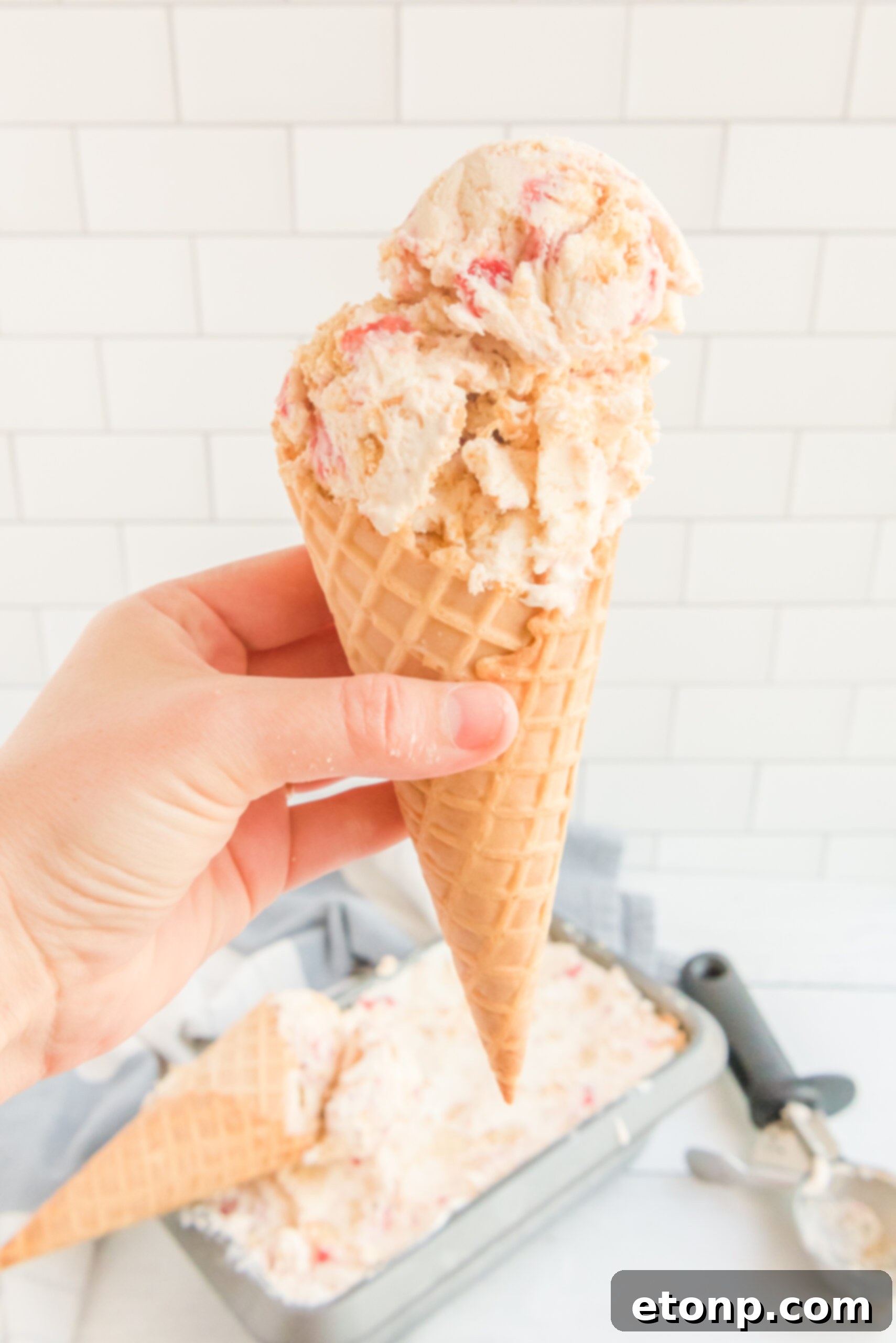 Front view of a waffle cone with a scoop of Strawberry Cheesecake Ice Cream.