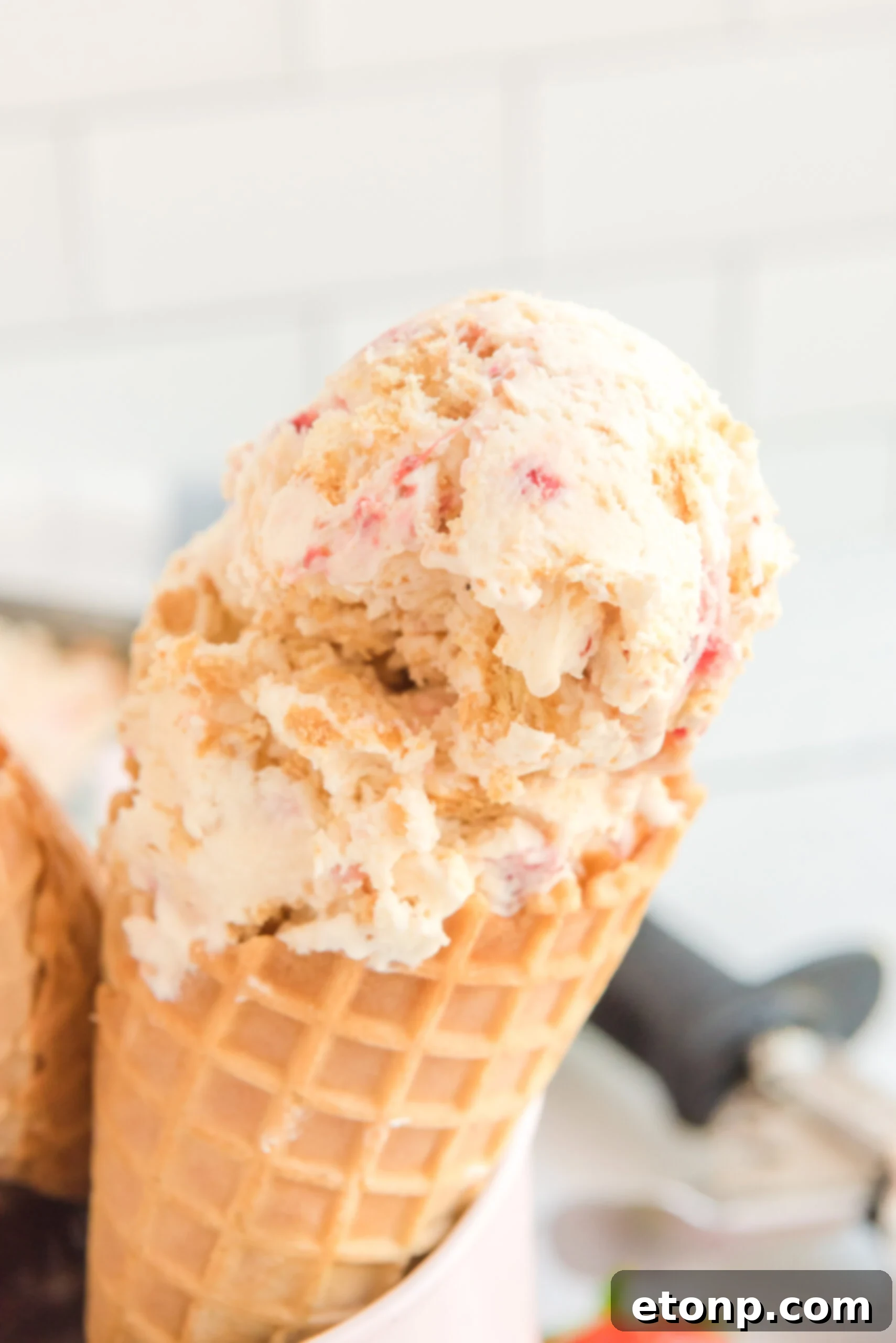 Close up view of a waffle cone with a scoop of Strawberry Cheesecake Ice Cream.