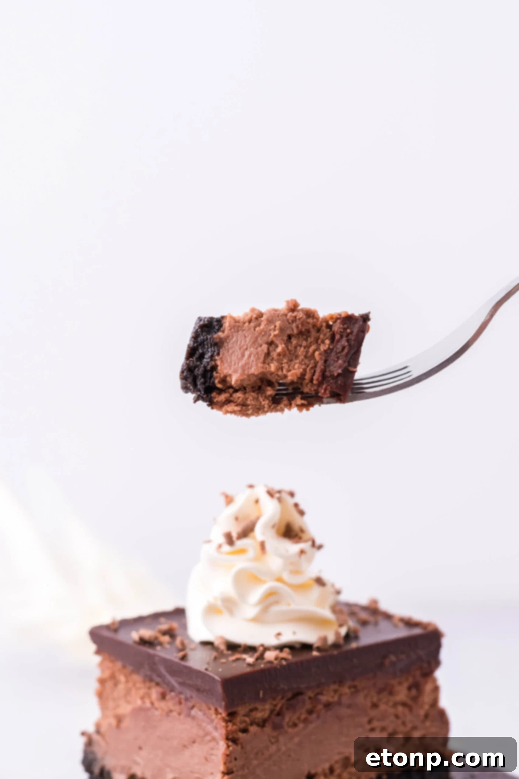 A bite of cheesecake on a silver fork with the cheesecake bars in the background. 