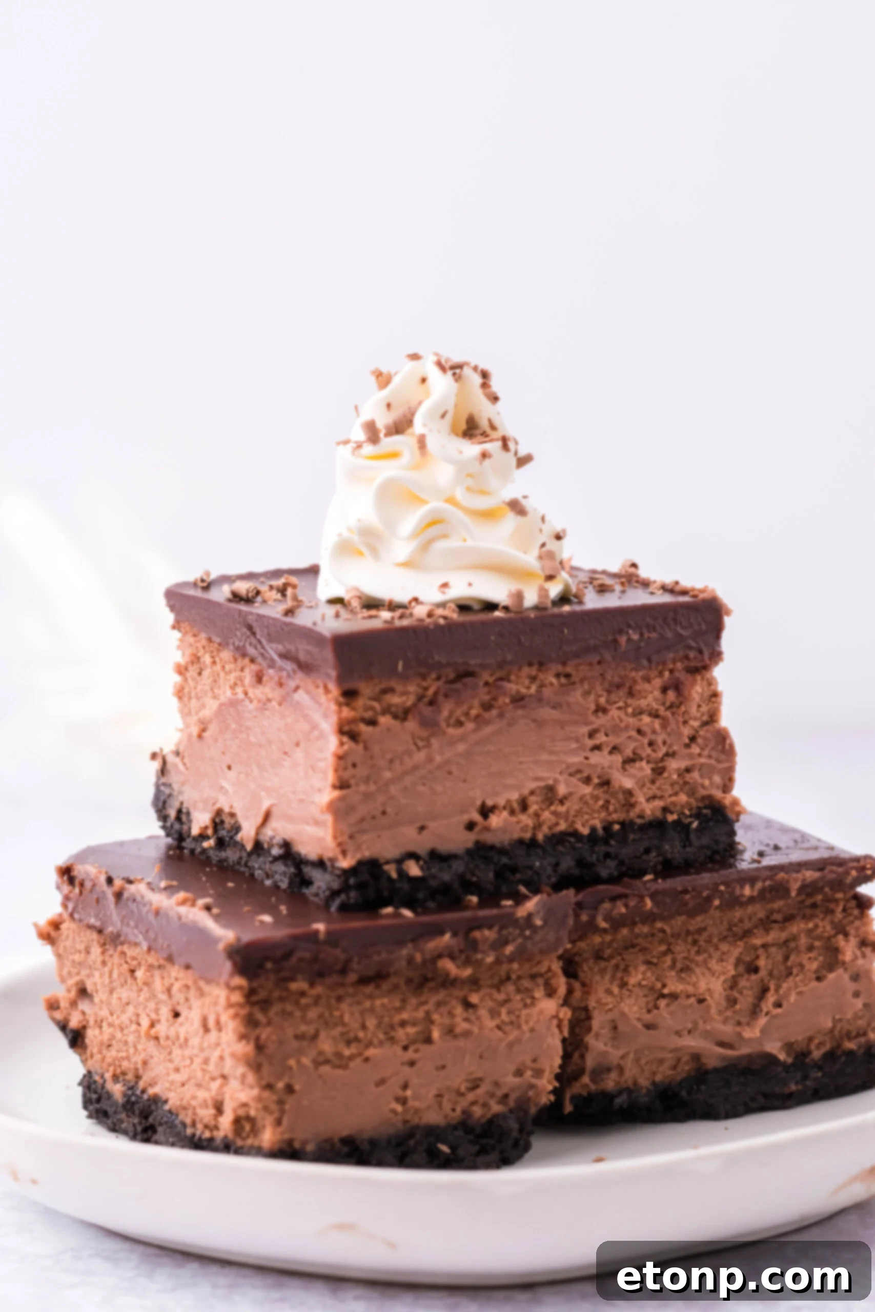 Three Chocolate Cheesecake bars topped on top of each other topped with whipped cream and chocolate shavings. 