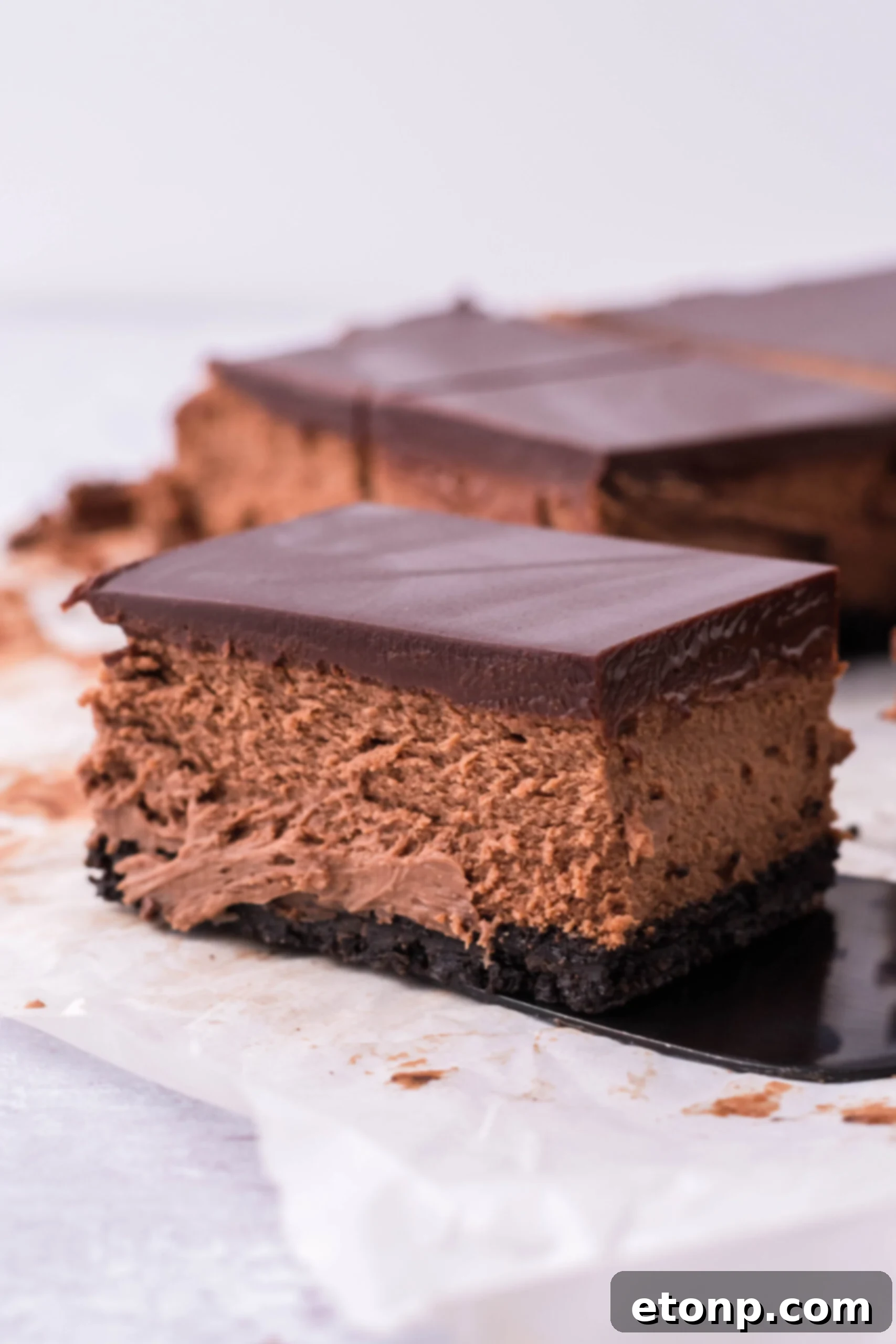 A bar of chocolate cheesecake being removed with a black spatula. 