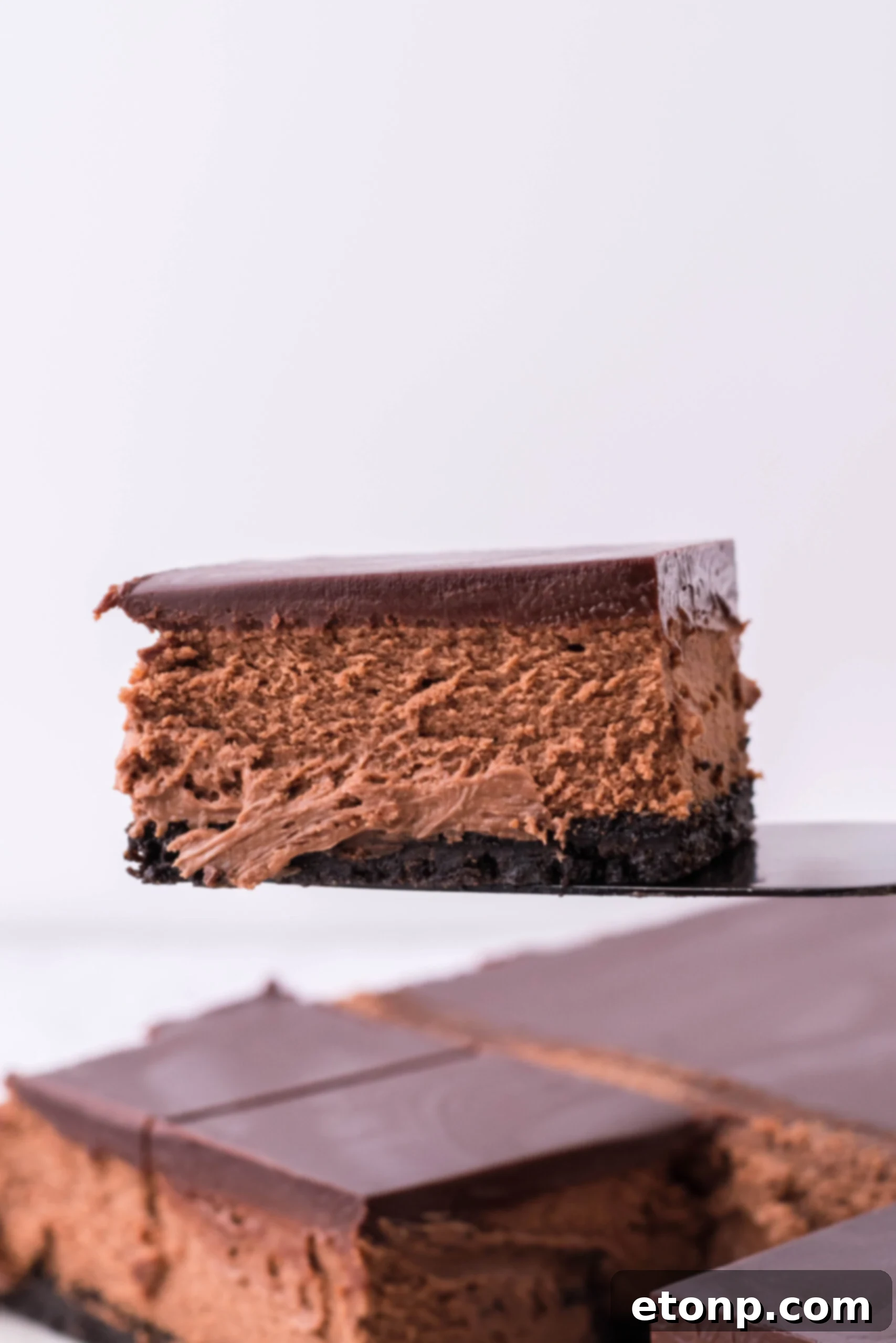 A black spatula picking up a bar of chocolate cheesecake. 