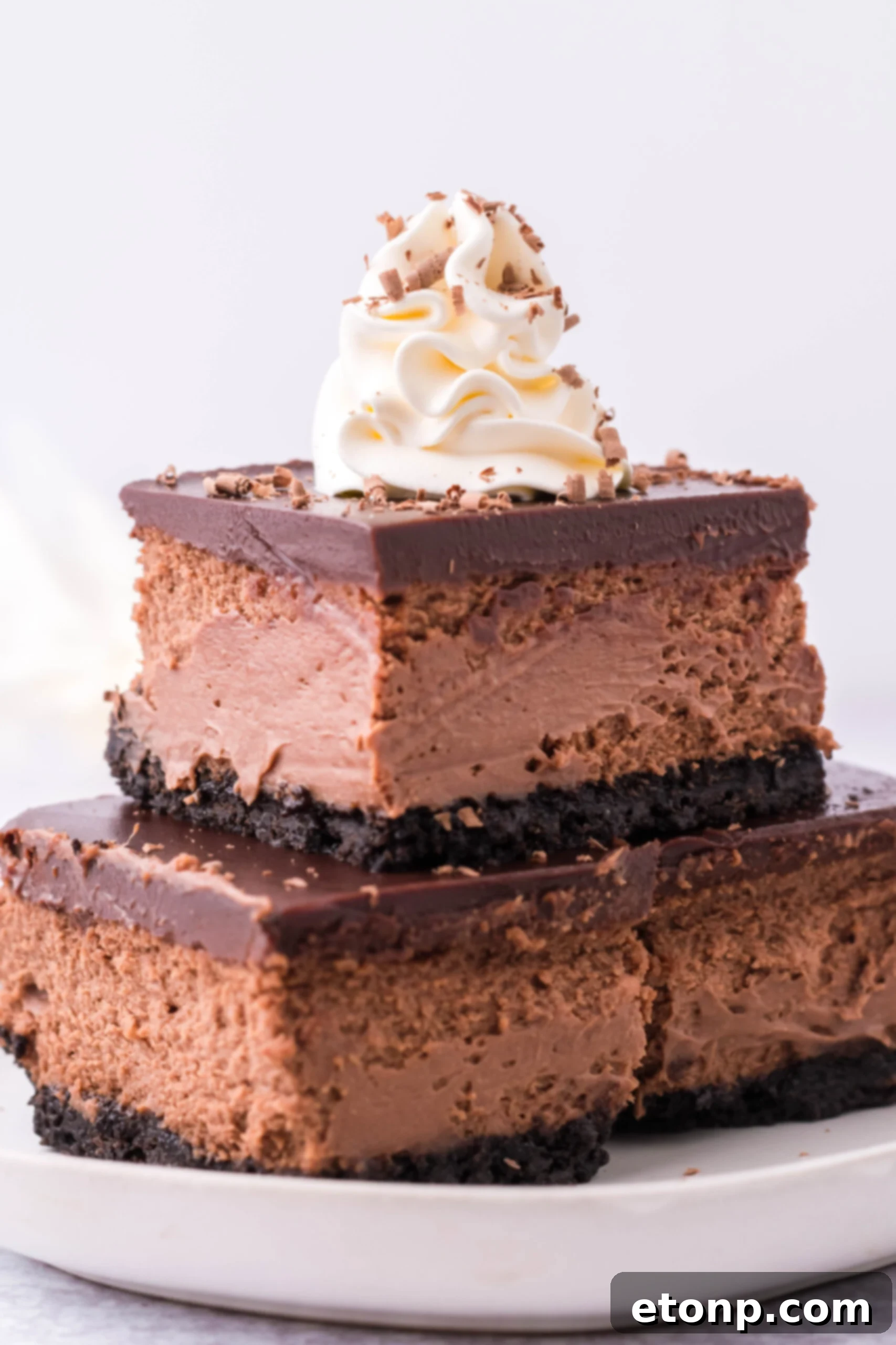 Three Chocolate Cheesecake bars topped on top of each other topped with whipped cream and chocolate shavings. 