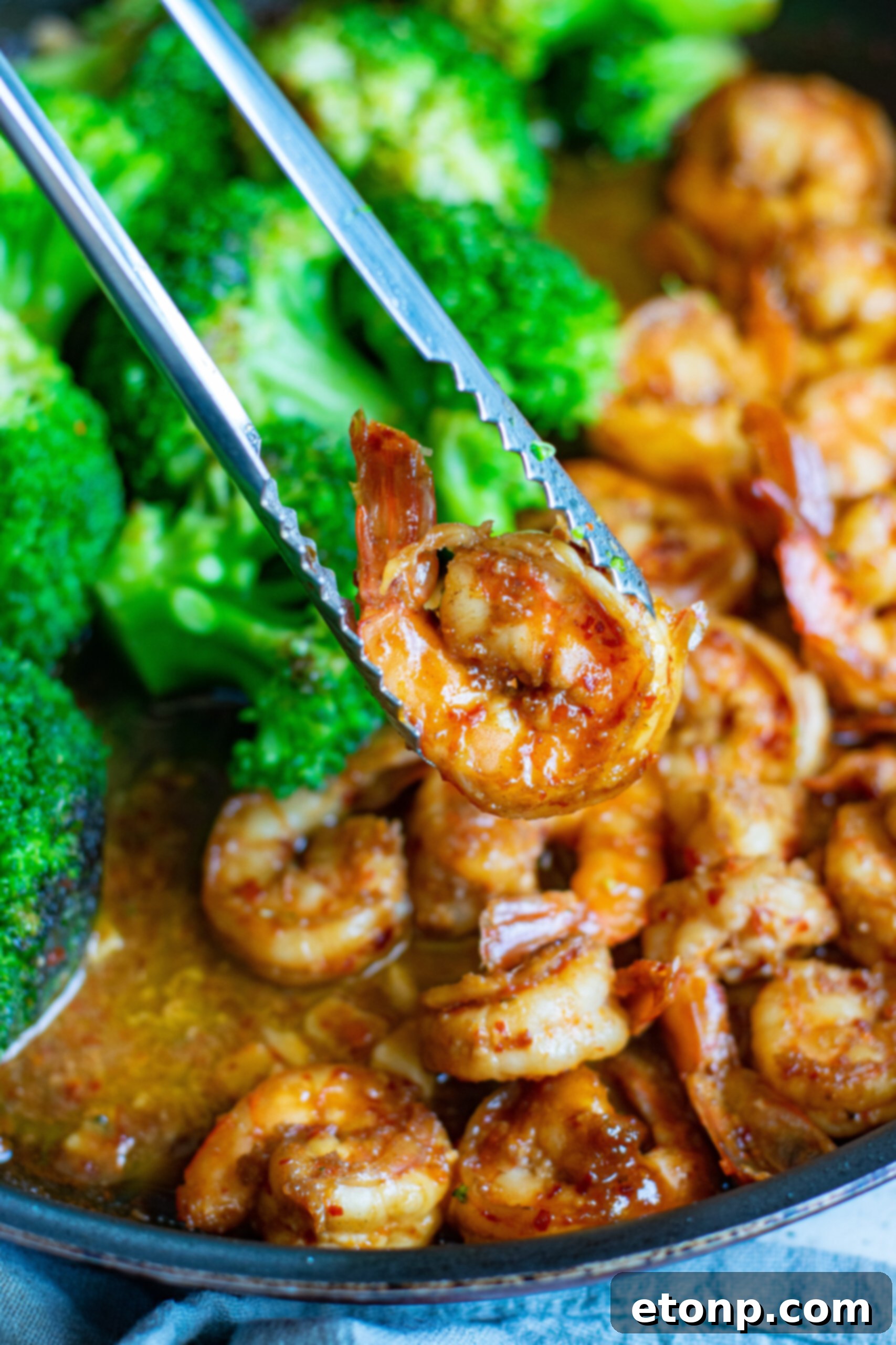 Garlic Shrimp and Broccoli Skillet 3 A pair of silver tongs removing a piece of shrimp from the skillet.