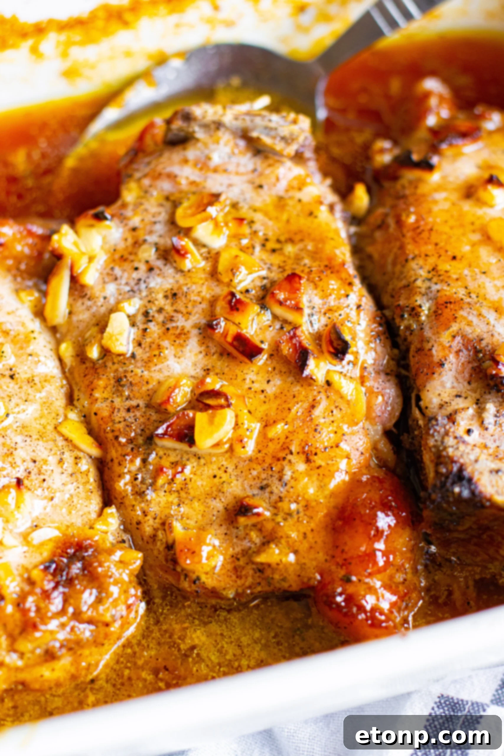 Close up view of Honey Garlic Pork Chops in a white baking dish, showing a perfectly cooked chop.