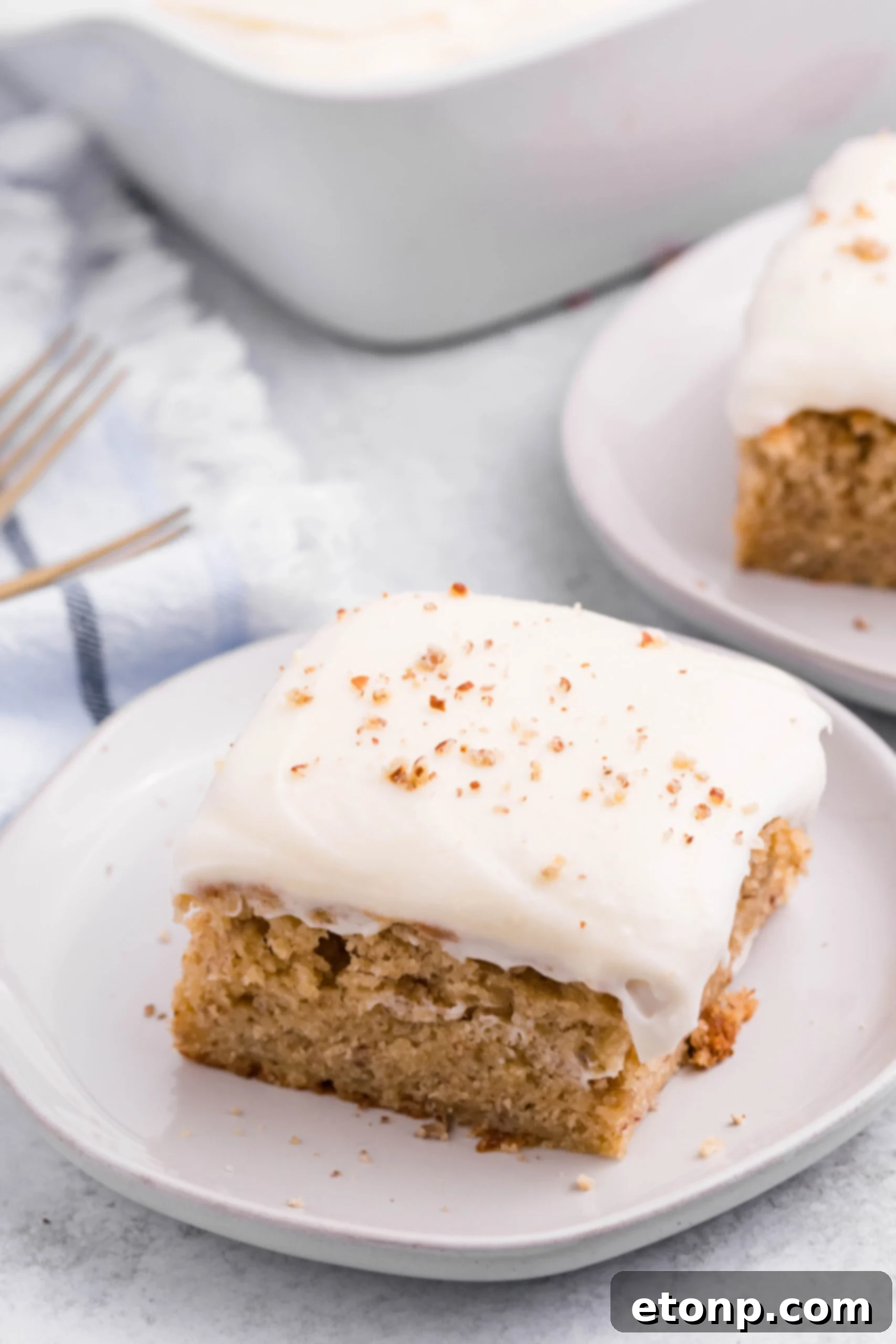 Close up view of a slice of Banana Sheet Cake on a white plate.