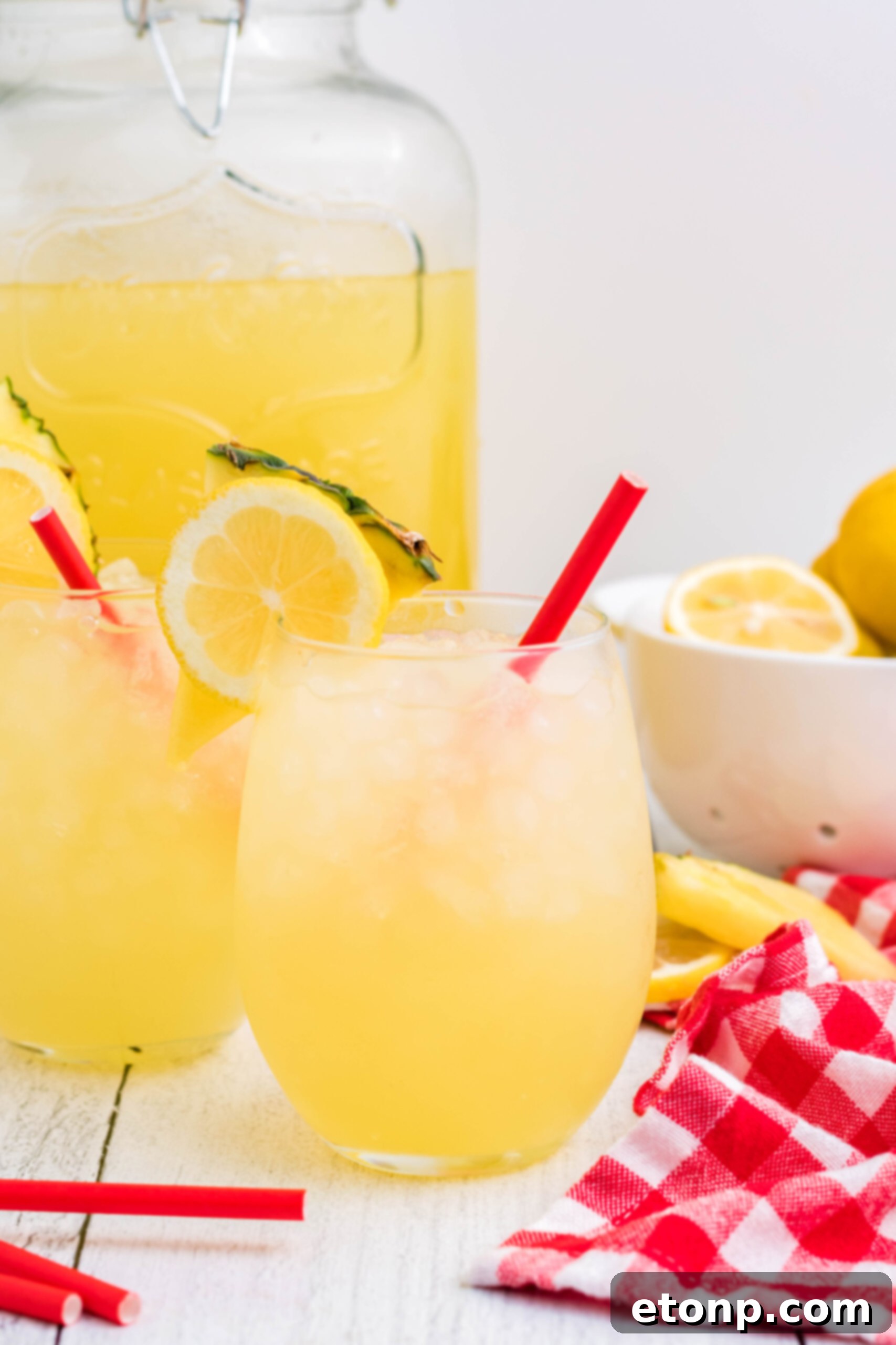 Front view of two glasses of Pineapple Vodka Lemonade, garnished with fresh lemon and pineapple slices.