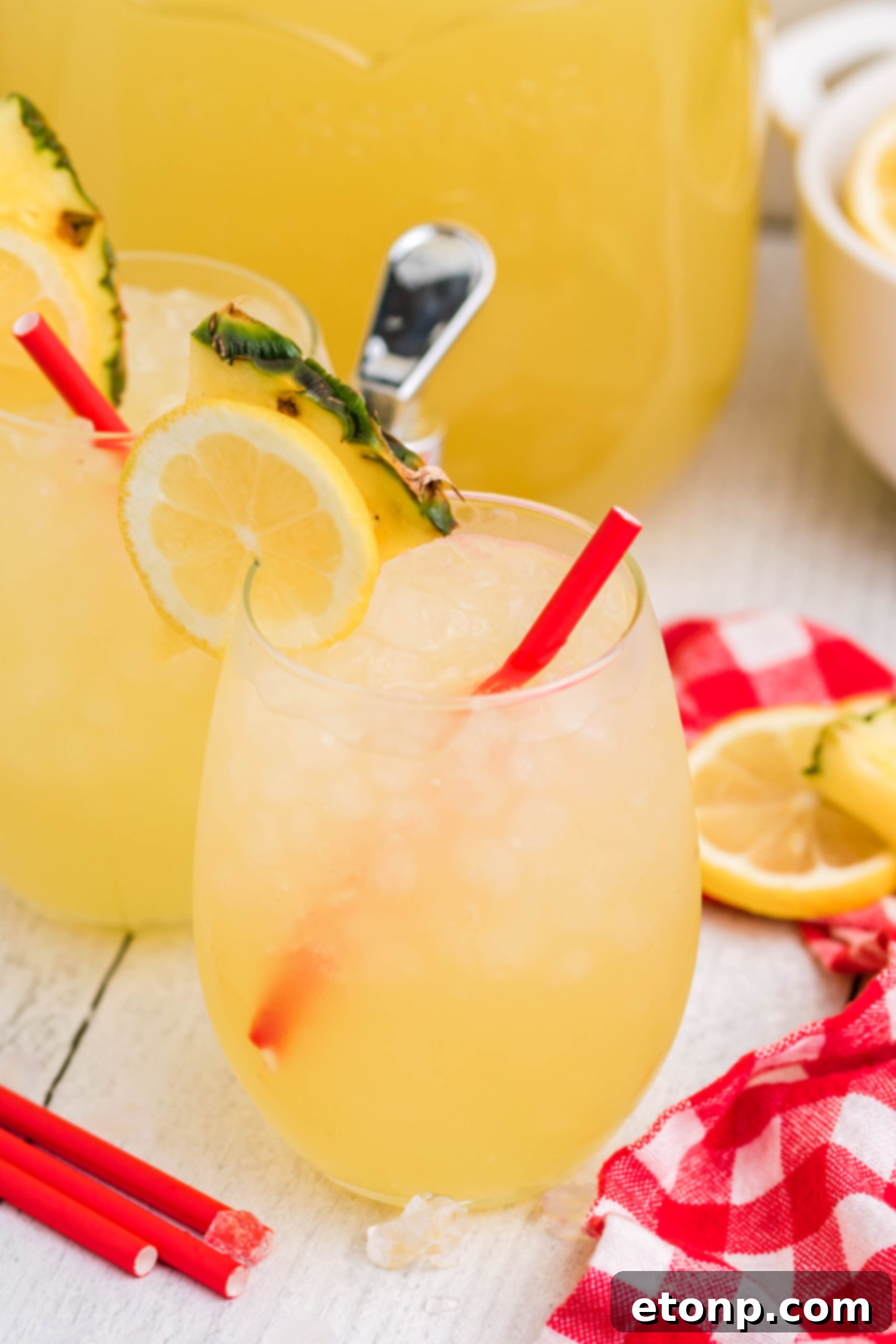 Front view of two glasses of Pineapple Vodka Lemonade garnished with a lemon and pineapple slice, glistening with condensation.