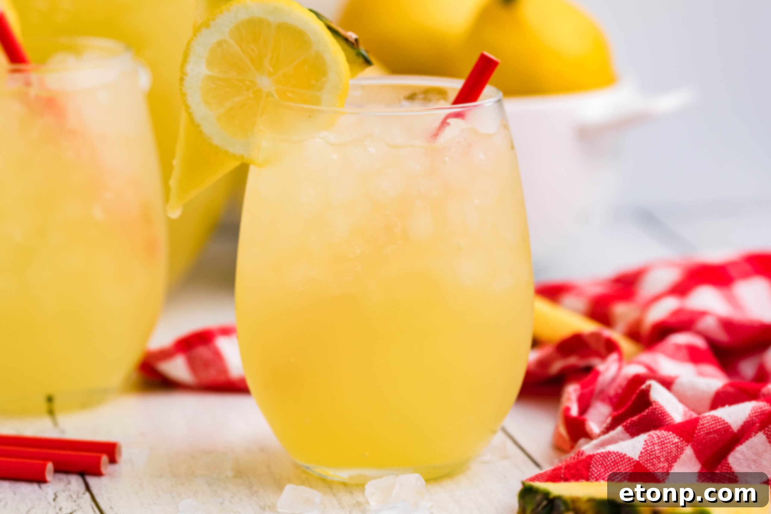 Front view of two glasses of Pineapple Vodka Lemonade garnished with a lemon and pineapple slice, with a wider shot of the table setting.