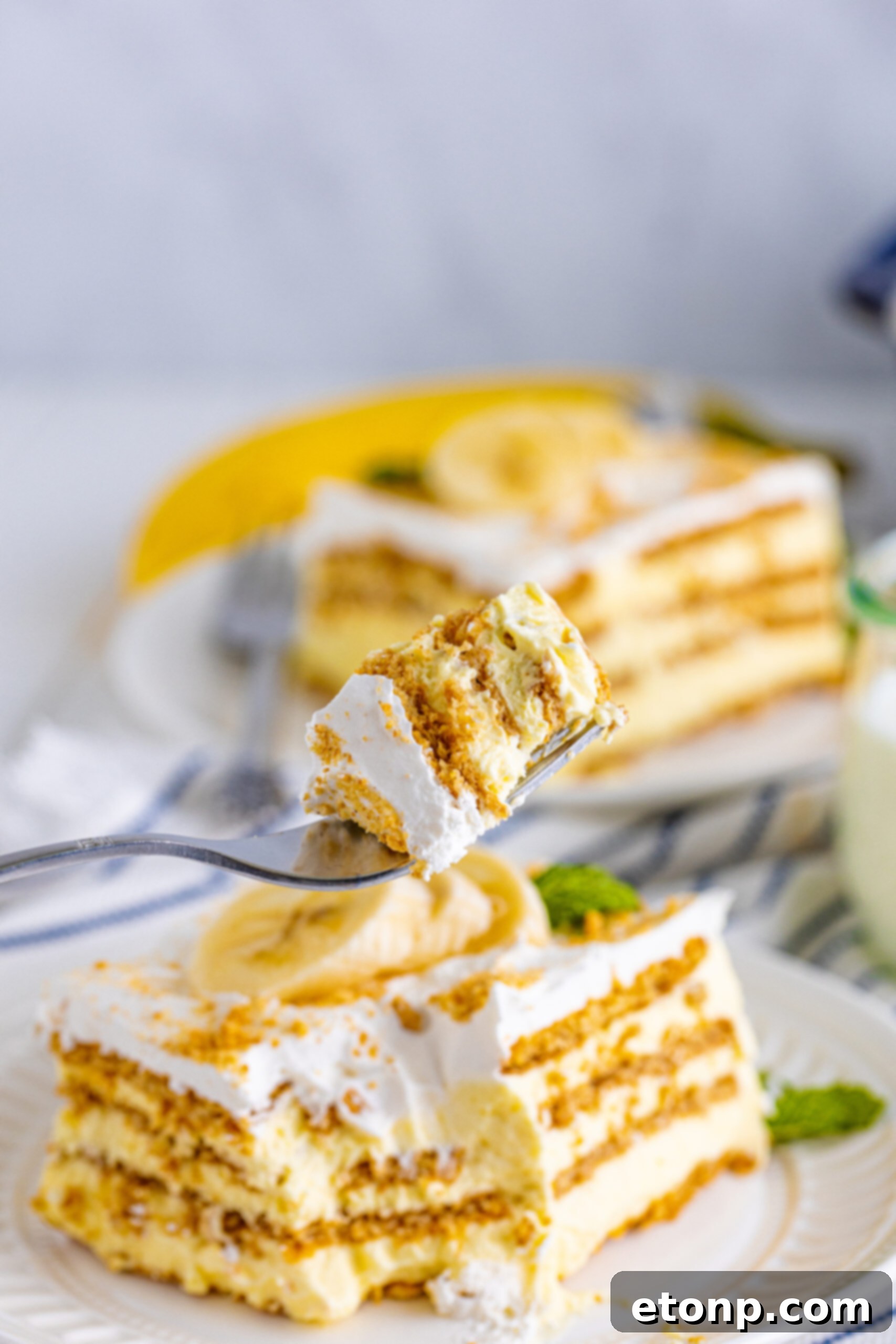 A close-up side view of a silver fork holding a perfect bite of Banana Icebox Cake, showcasing the distinct layers and soft consistency.