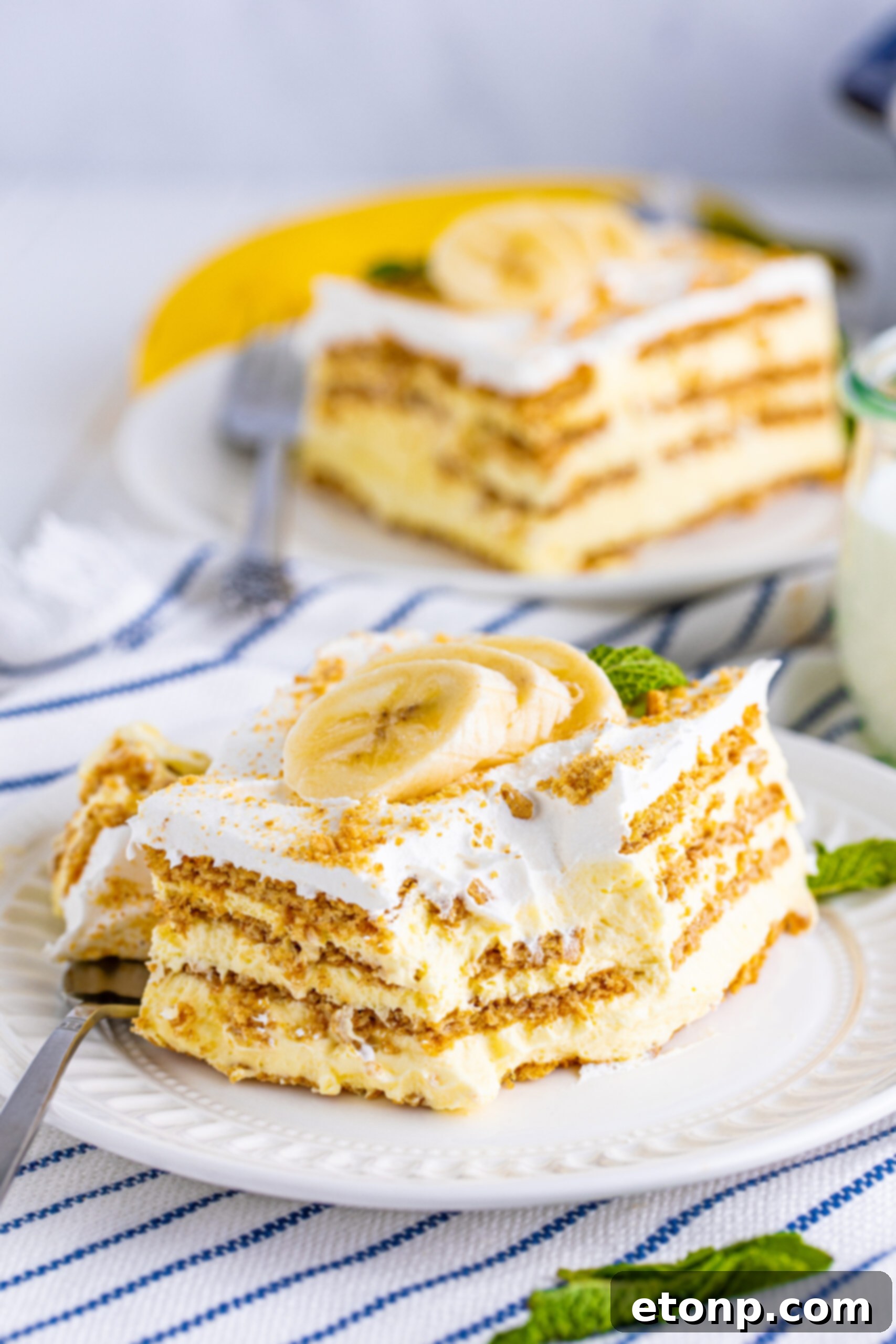 A final close-up of a delightful slice of Banana Icebox Cake on a white plate, with a fork having already taken a small bite, inviting further indulgence.
