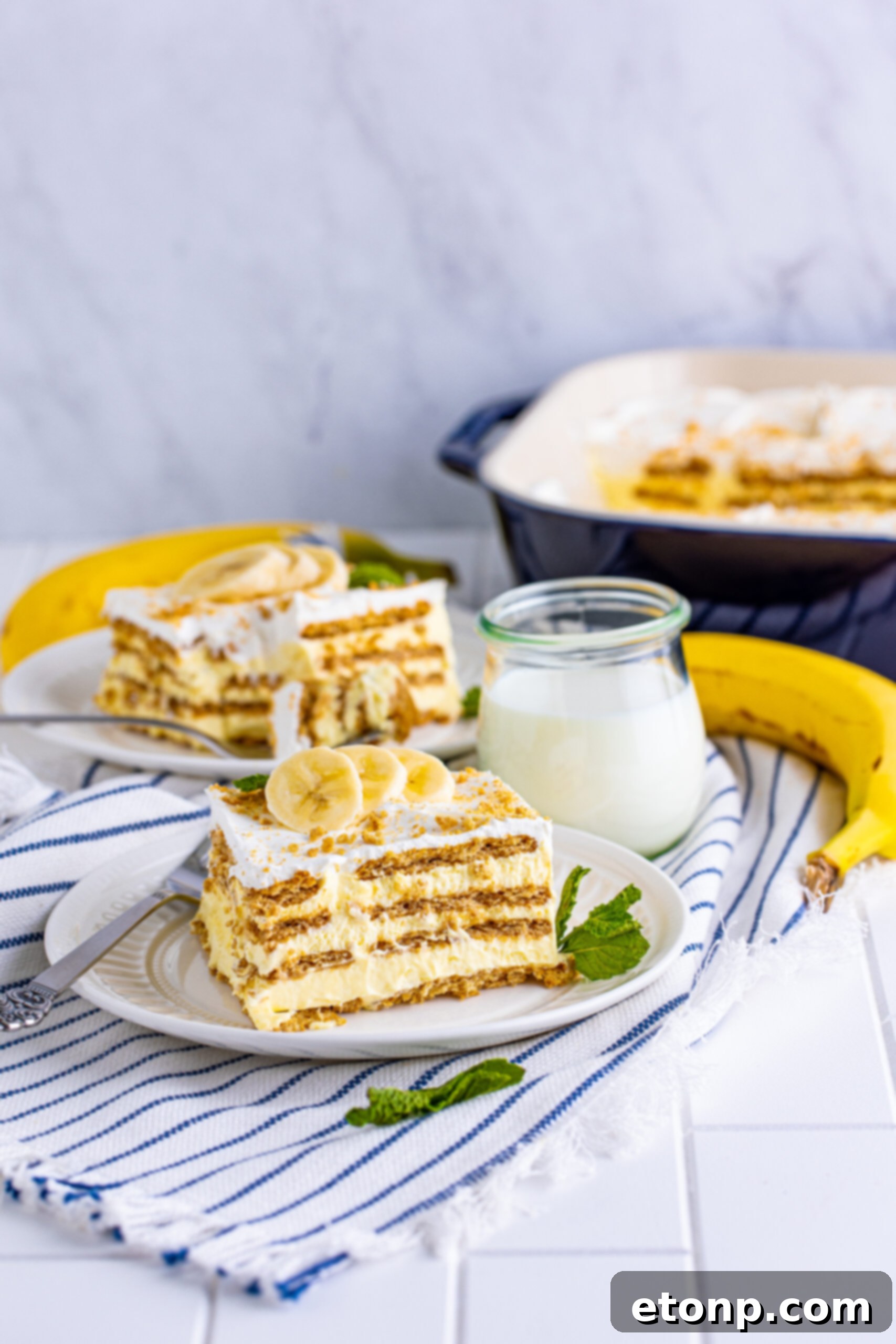 A close-up front view of a delicious slice of Banana Icebox Cake, featuring a perfectly balanced ratio of creamy layers and softened cookie, served on a white plate.