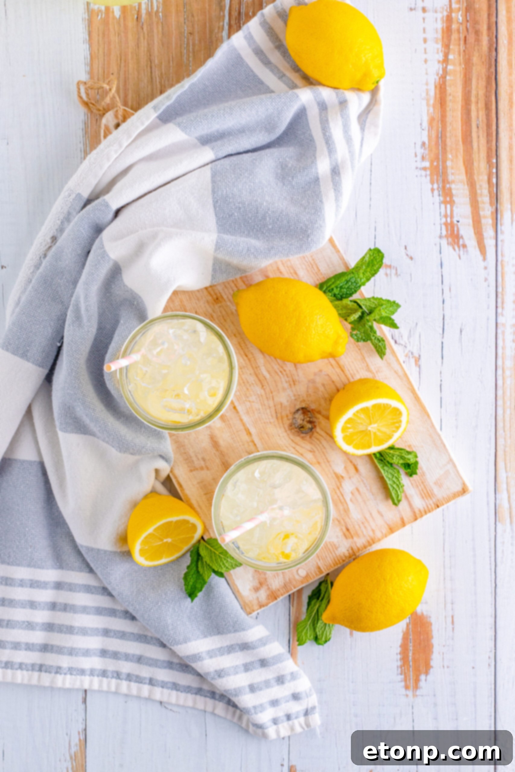 Overhead view of homemade lemonade in two mason jars, presented on a rustic wooden cutting board with lemon slices.