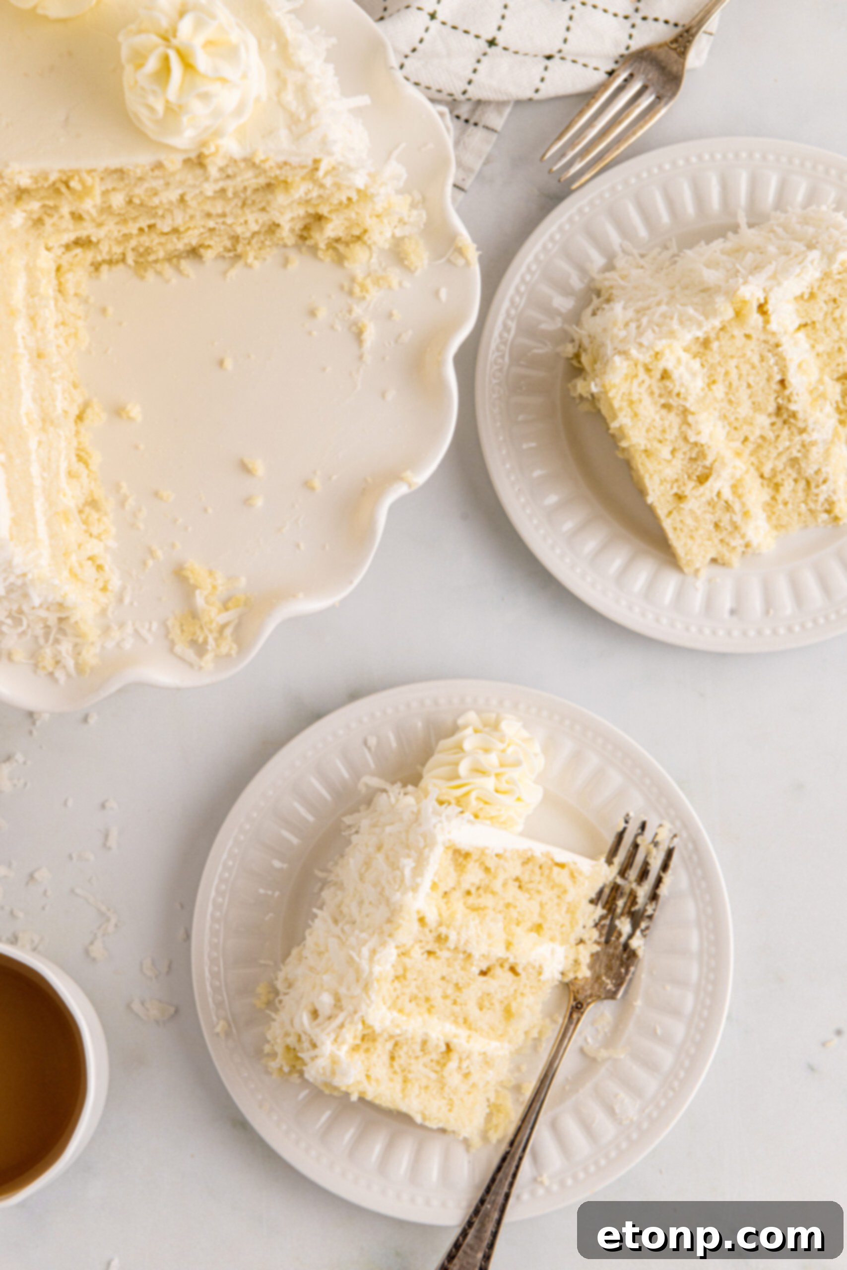 Overhead view of a slice of Coconut Layer Cake on a white plate with a bite removed by a silver fork, highlighting the layered beauty and deliciousness.