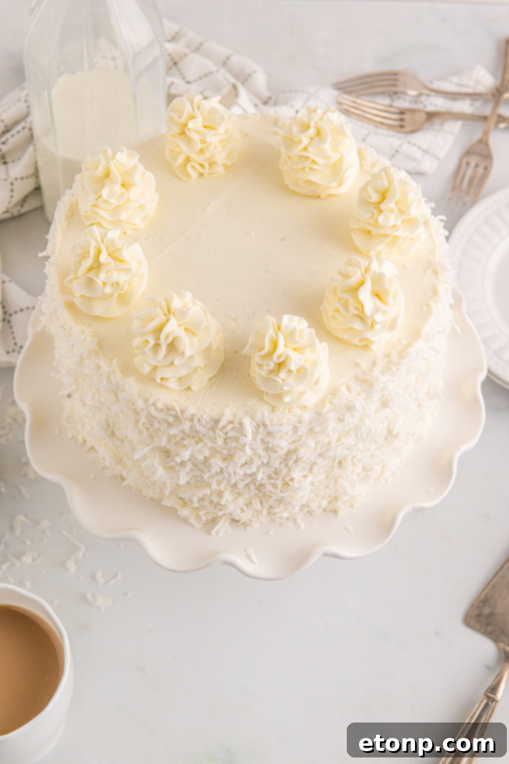 Overhead view of a beautifully frosted Coconut Layer Cake on a white cake stand, highlighting its intricate design and inviting texture.