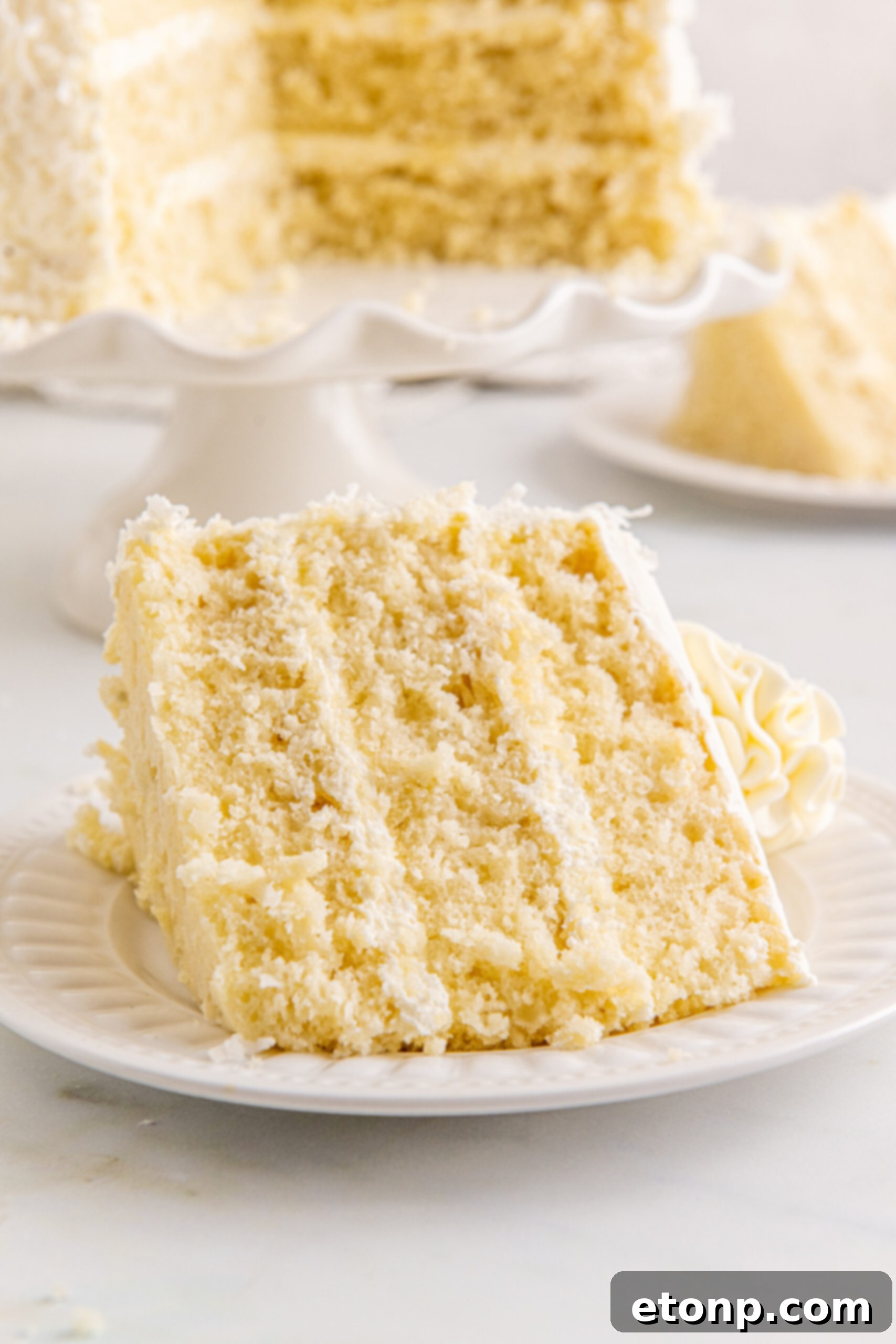 Front view of a perfect slice of Coconut Layer Cake served on a white plate, ready to be enjoyed.