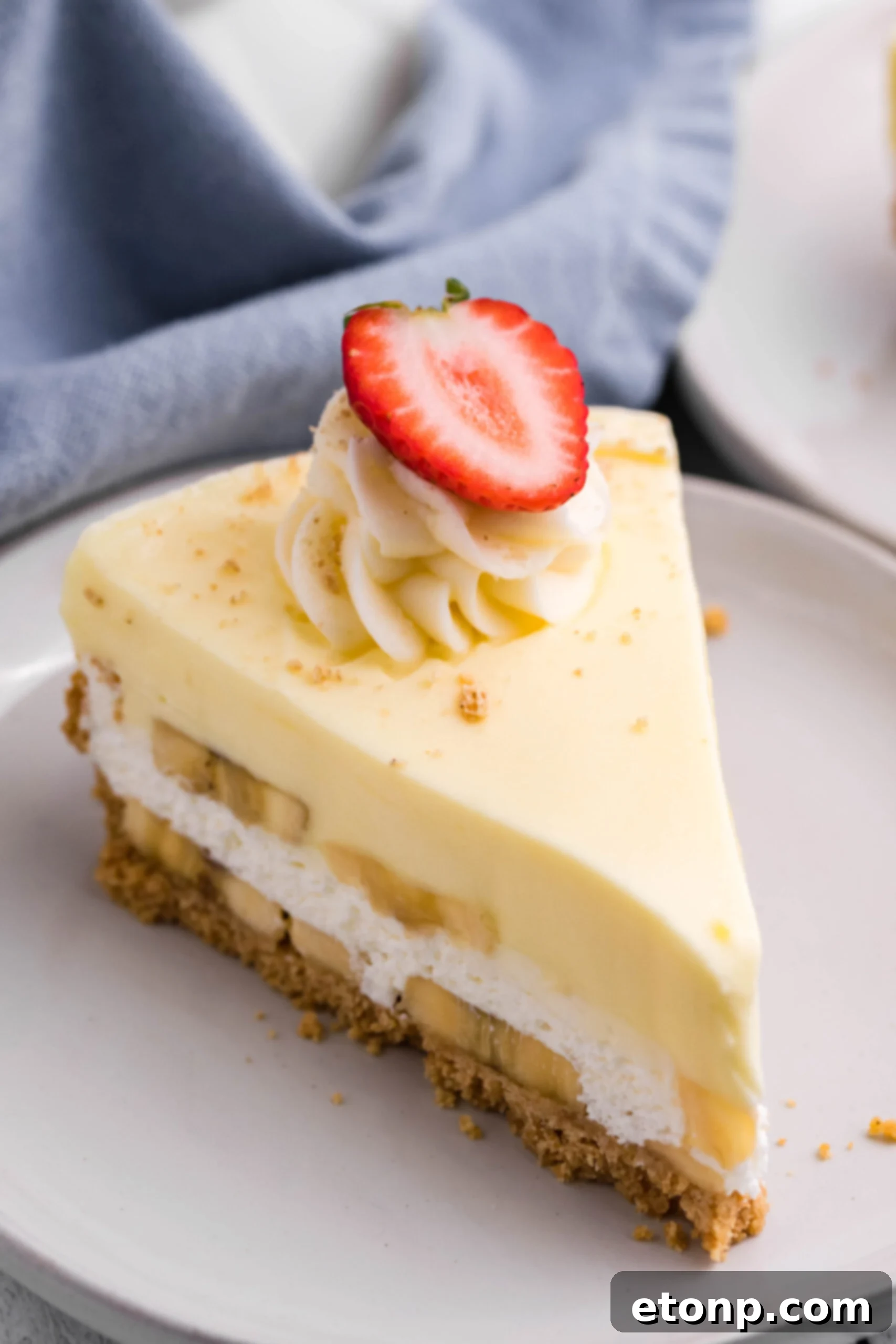 Front view of a slice of Banana Cream Cheesecake on a white plate, showing the distinct layers and a hint of the fresh bananas.