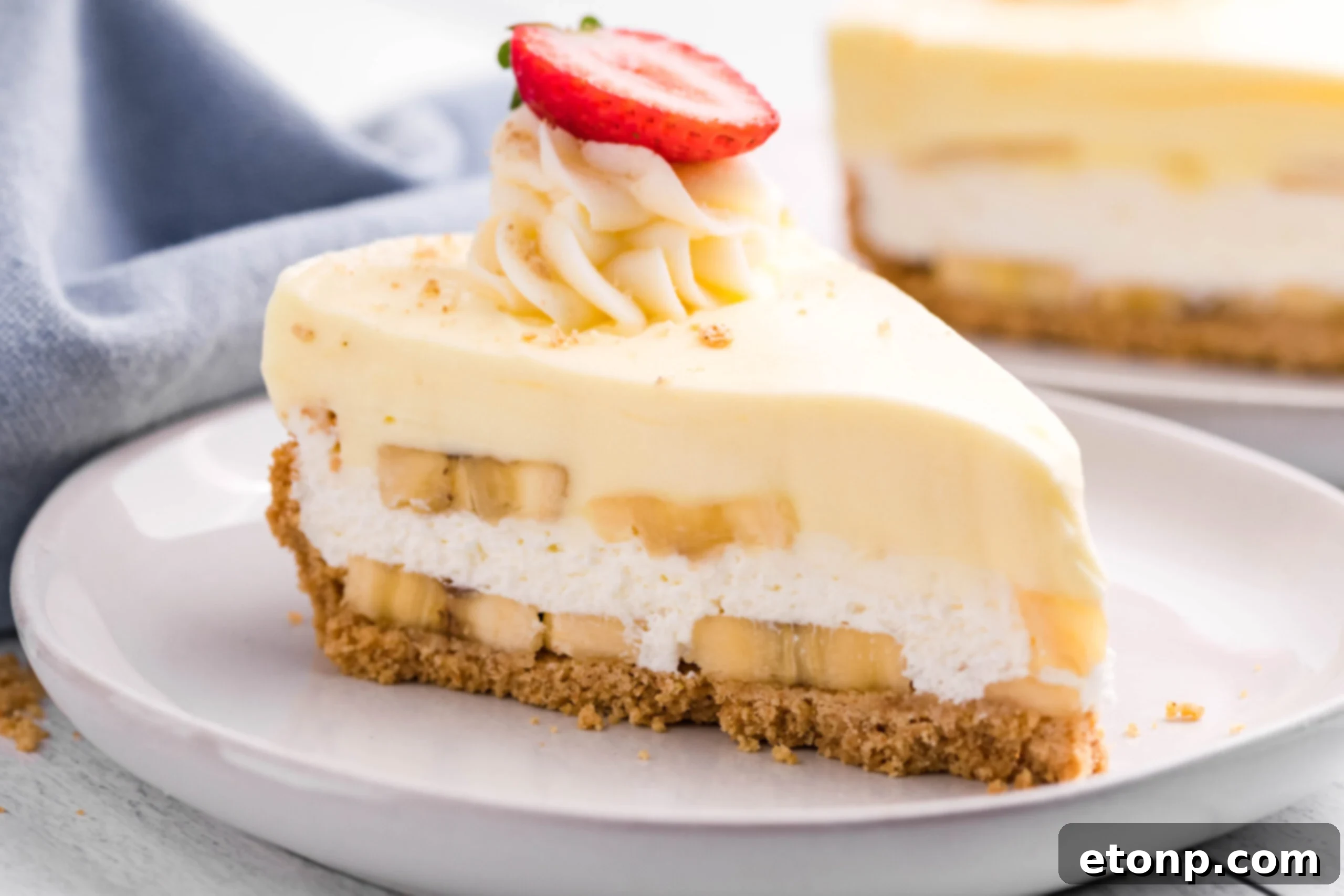 Side view of a slice of Banana Cream Cheesecake on a white plate, showcasing the various layers from crust to creamy topping.