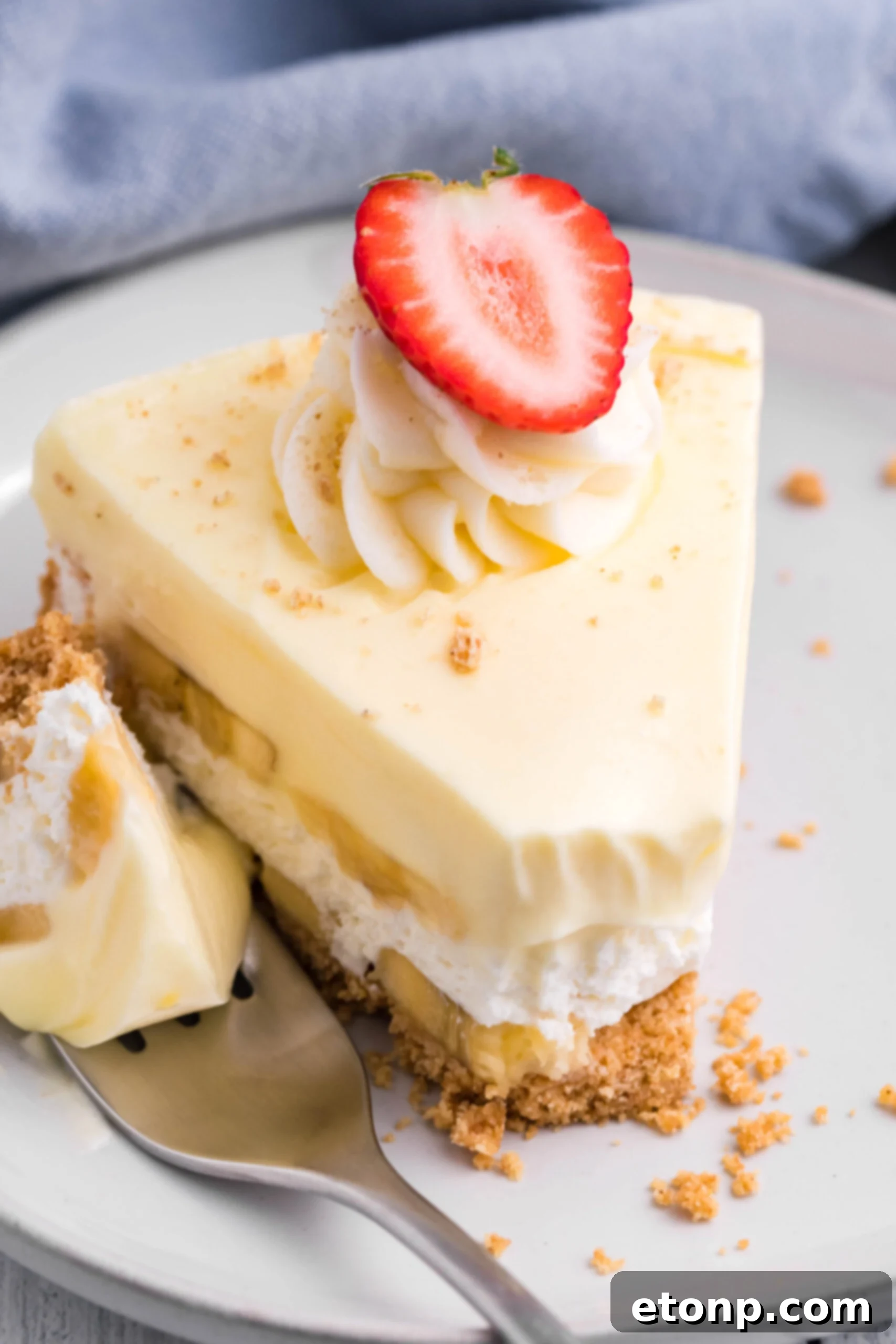 Front view of a slice of Banana Cream Cheesecake on a white plate with a bite removed by a silver fork, highlighting the delicious filling.