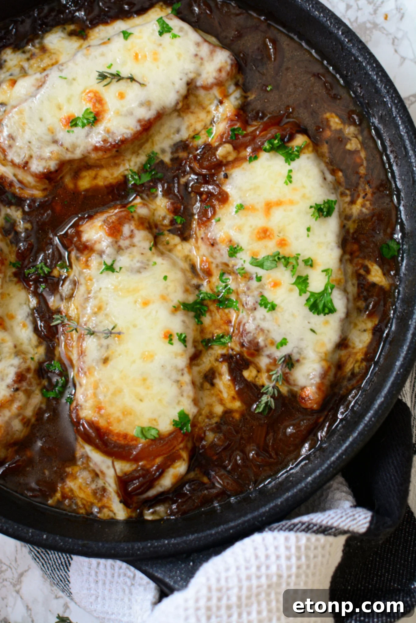 Close-up view of a cast iron skillet filled with golden brown French Onion Pork Chops, generously topped with melted provolone cheese and rich caramelized onion gravy.