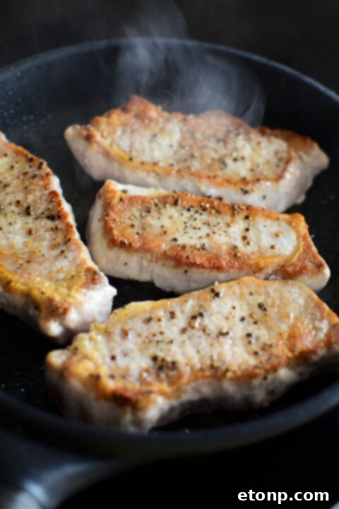 Side view of a pork chop being coated in a creamy Dijon mustard before baking.
