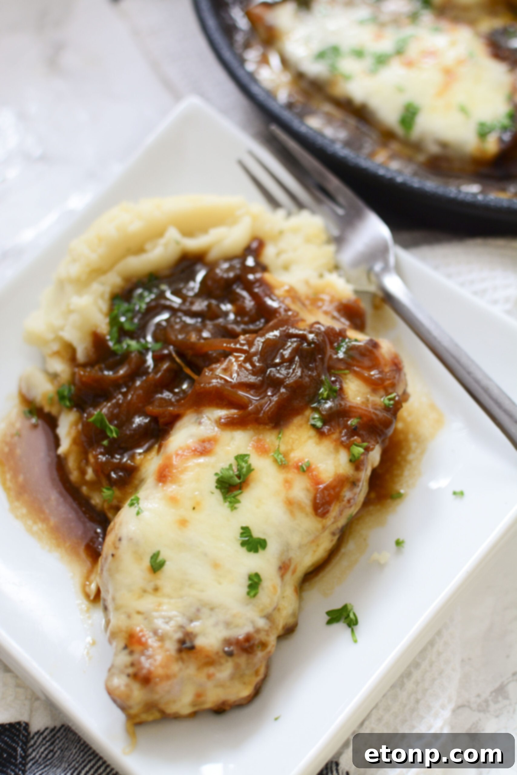 Close-up of a serving of French Onion Pork Chops on a white plate with mashed potatoes, showcasing the rich texture of the gravy and the tender pork.