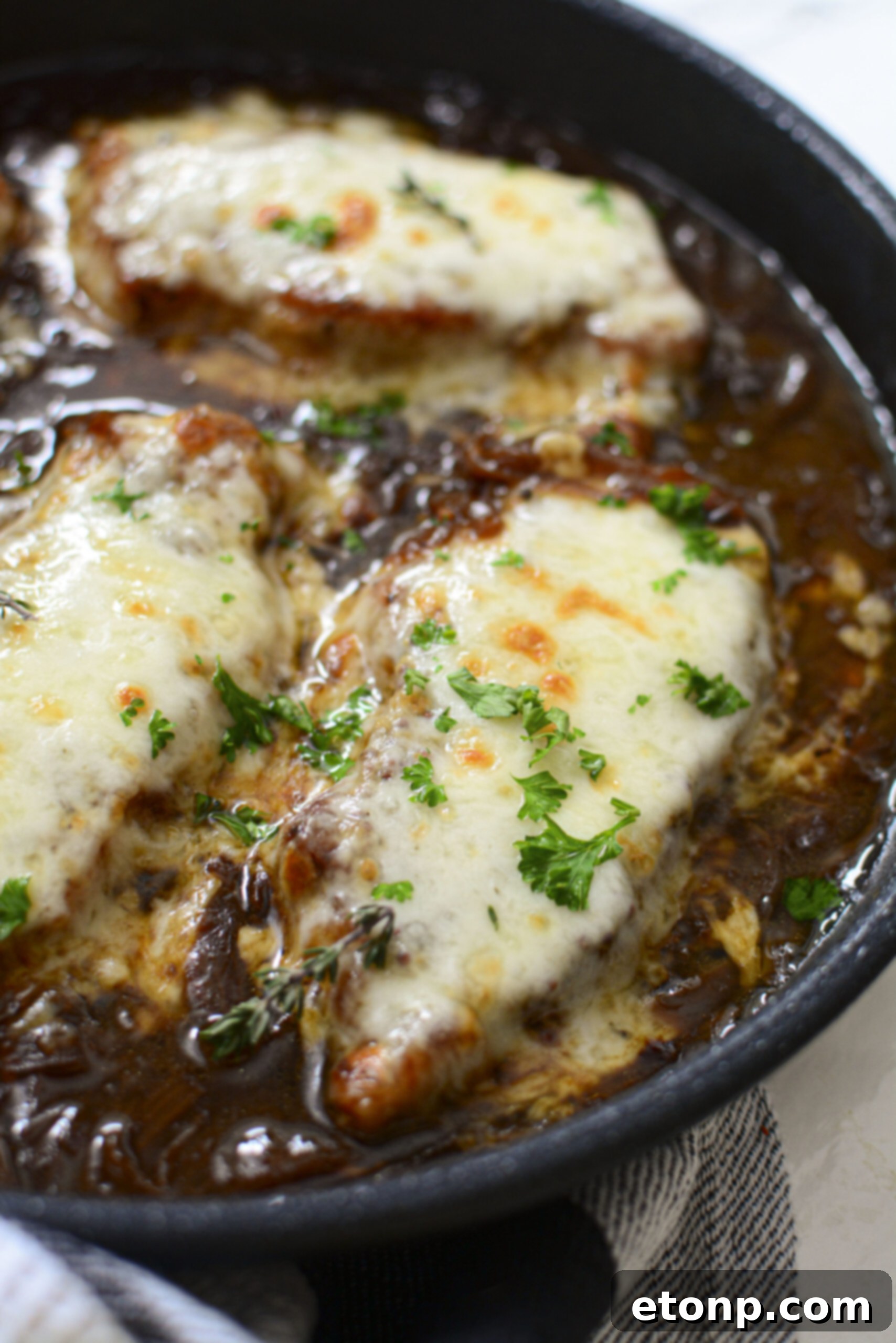 Two French Onion Pork Chops resting in a bubbling, deep brown onion gravy within a rustic cast iron skillet, ready to be served.