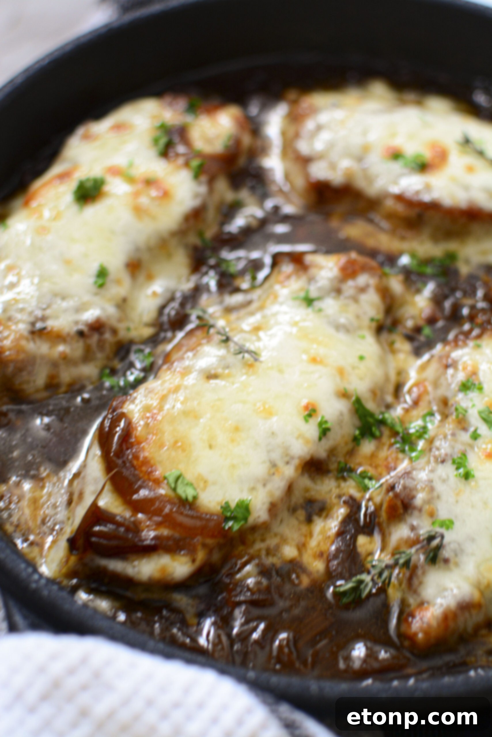 A top-down perspective of French Onion Pork Chops in a cast iron skillet, showcasing the melted cheese, tender pork, and rich, glistening onion sauce.