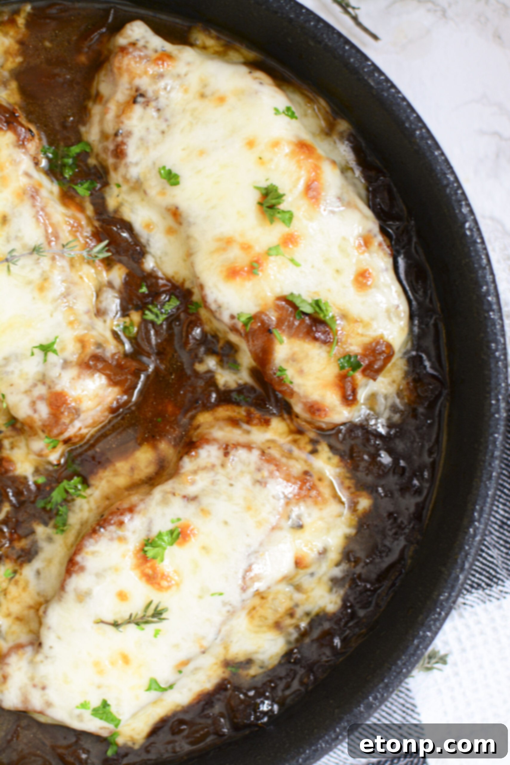 Overhead shot capturing the delectable French Onion Pork Chops in a cast iron pan, highlighting the perfectly browned pork and cheese, with a generous serving of onion gravy.