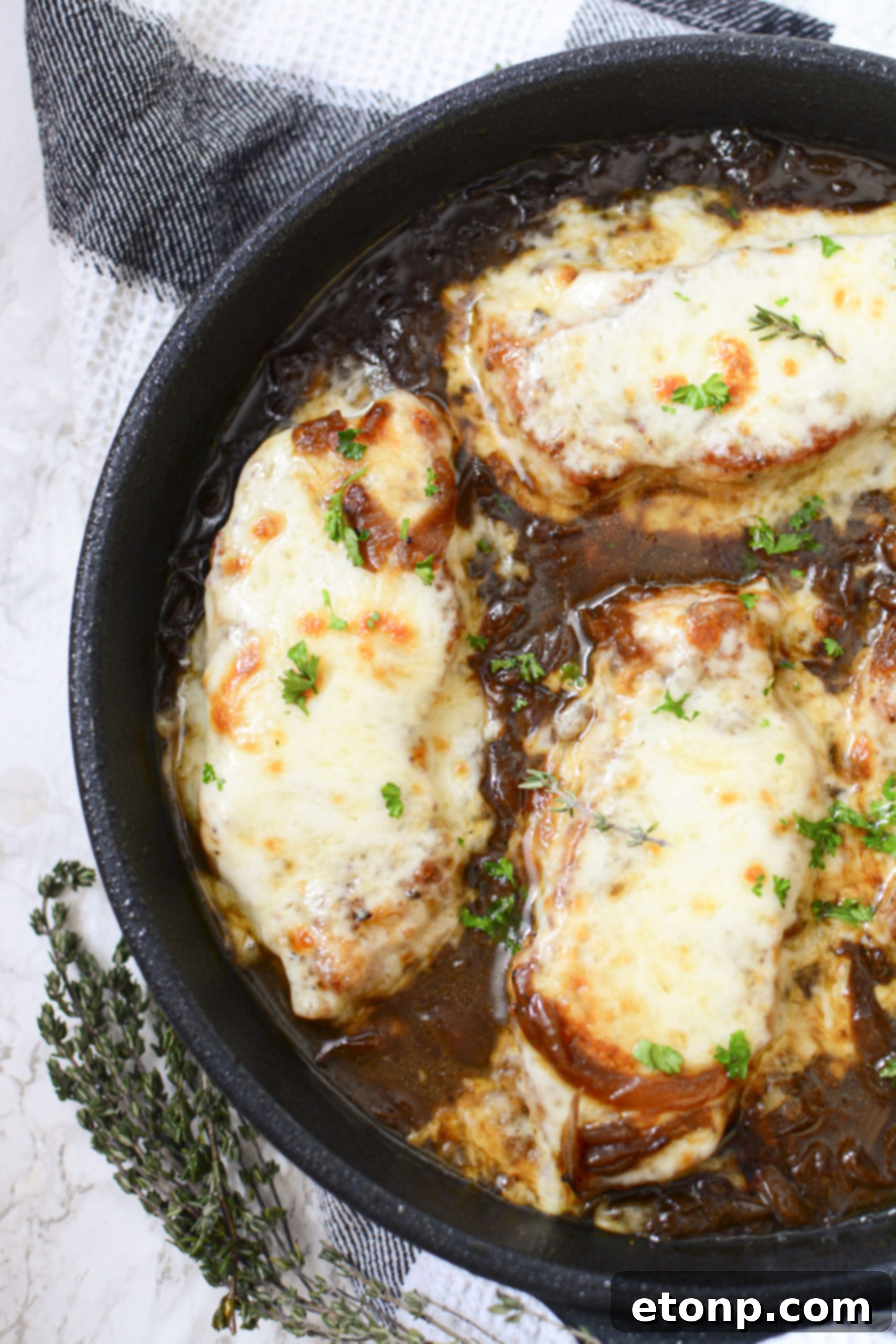 Overhead view of French Onion Pork Chops with a bubbling, golden cheese crust and rich gravy, fresh out of the oven in a cast iron skillet.
