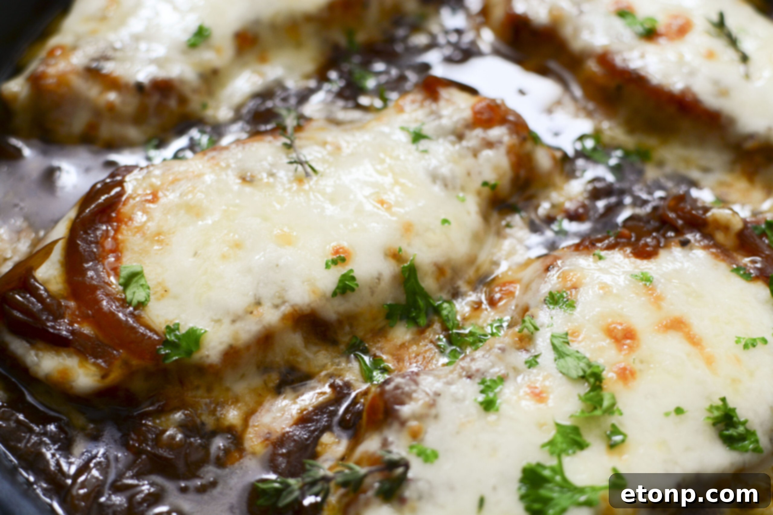 Close-up of French Onion Pork Chops in a cast iron skillet, with a focus on the rich, glossy onion gravy and perfectly melted cheese, ready to be served.