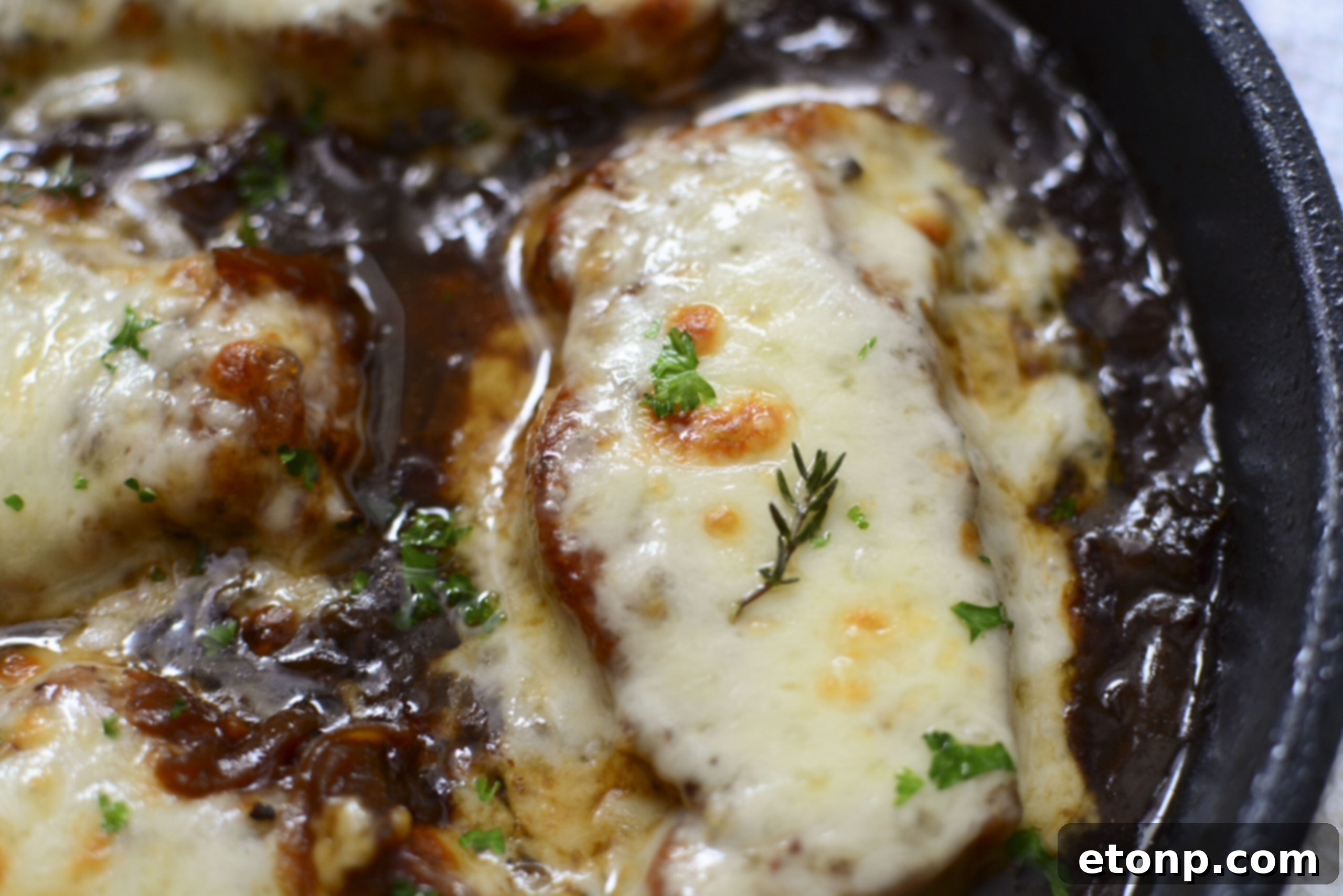Overhead view of multiple French Onion Pork Chops nestled in a cast iron skillet, each topped with a golden layer of melted cheese and surrounded by a savory onion gravy.
