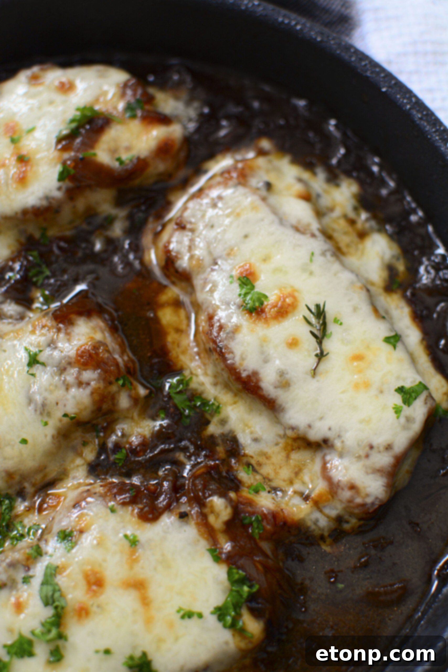 Overhead shot of French Onion Pork Chops resting in a cast iron skillet, adorned with a golden-brown melted cheese topping and swimming in a rich, dark onion gravy.