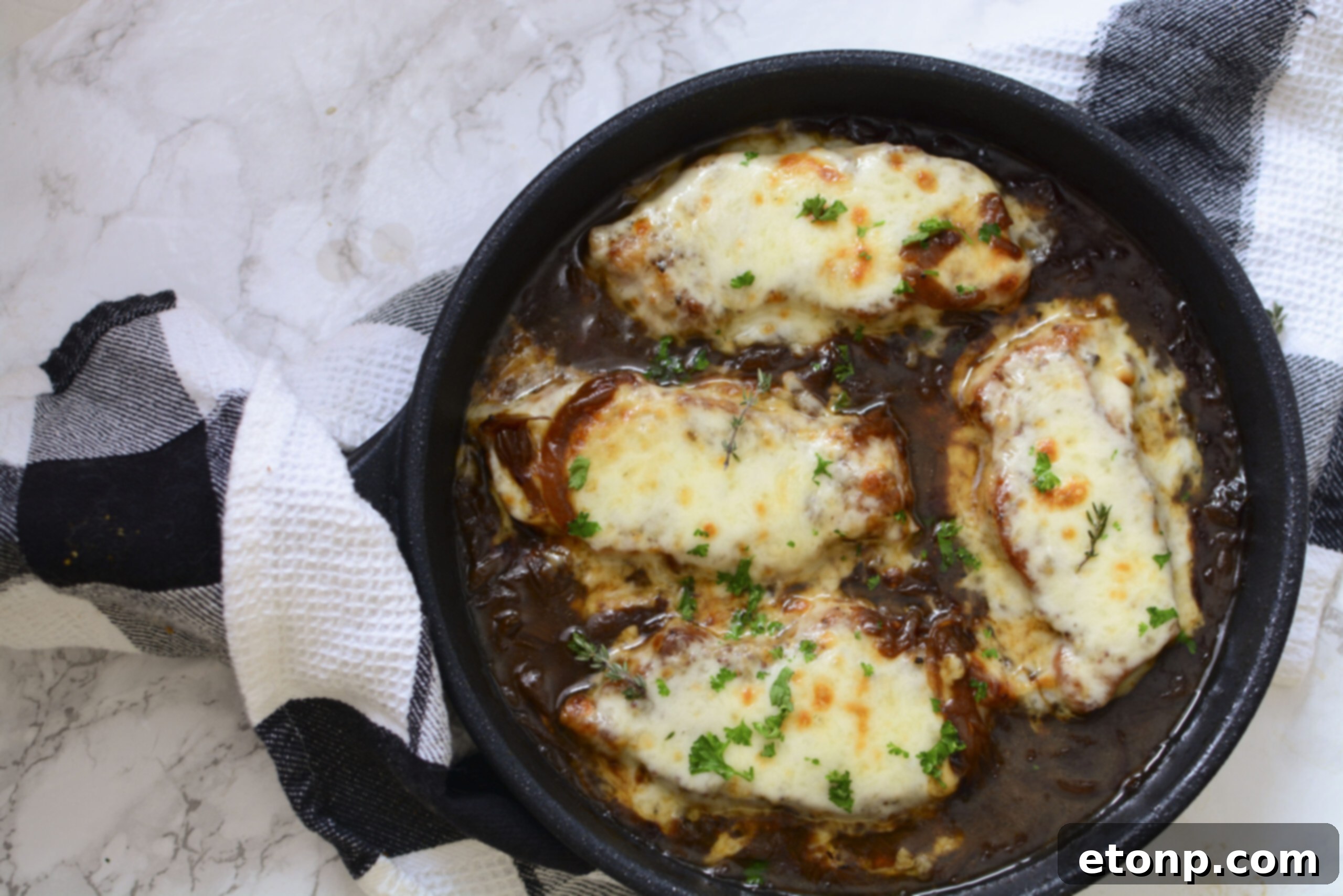 Overhead perspective of French Onion Pork Chops in a cast iron skillet, showing a perfect sear on the pork, a glossy onion sauce, and bubbly melted provolone cheese.