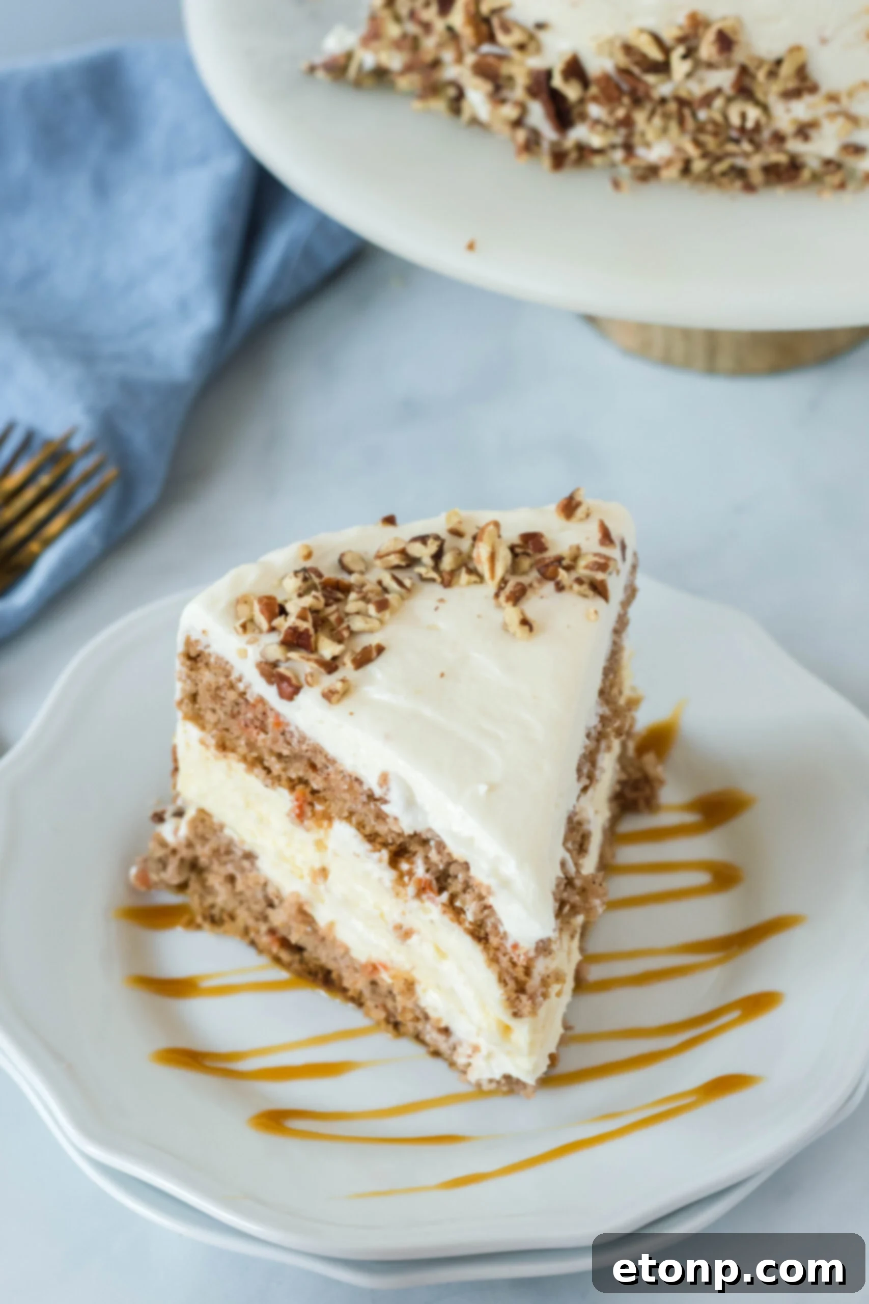 Front view of a slice of Carrot Cake Cheesecake on a white plate drizzled with caramel.