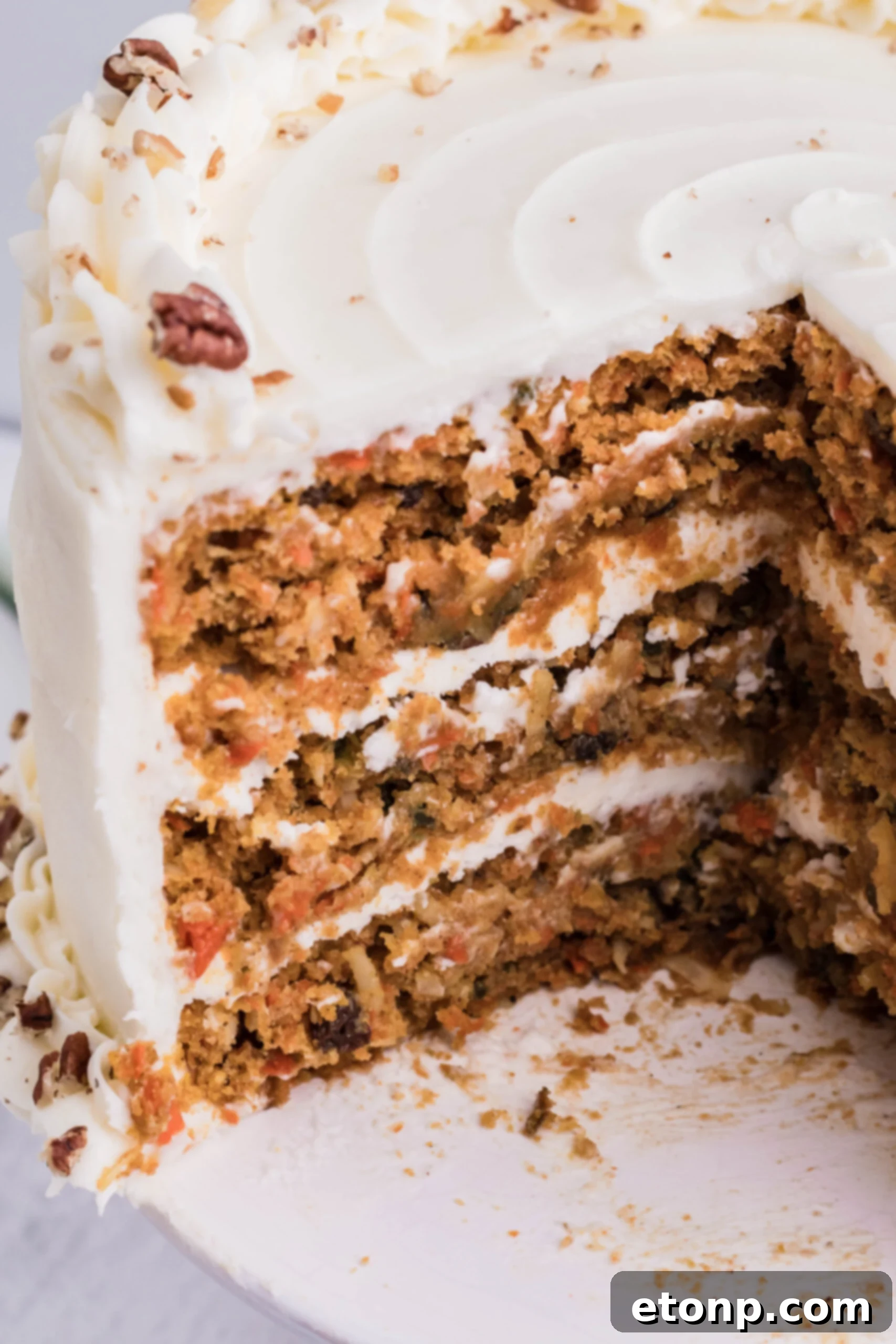 A beautifully frosted homemade carrot cake on a white cake stand with two slices already removed, revealing the moist, spiced interior.