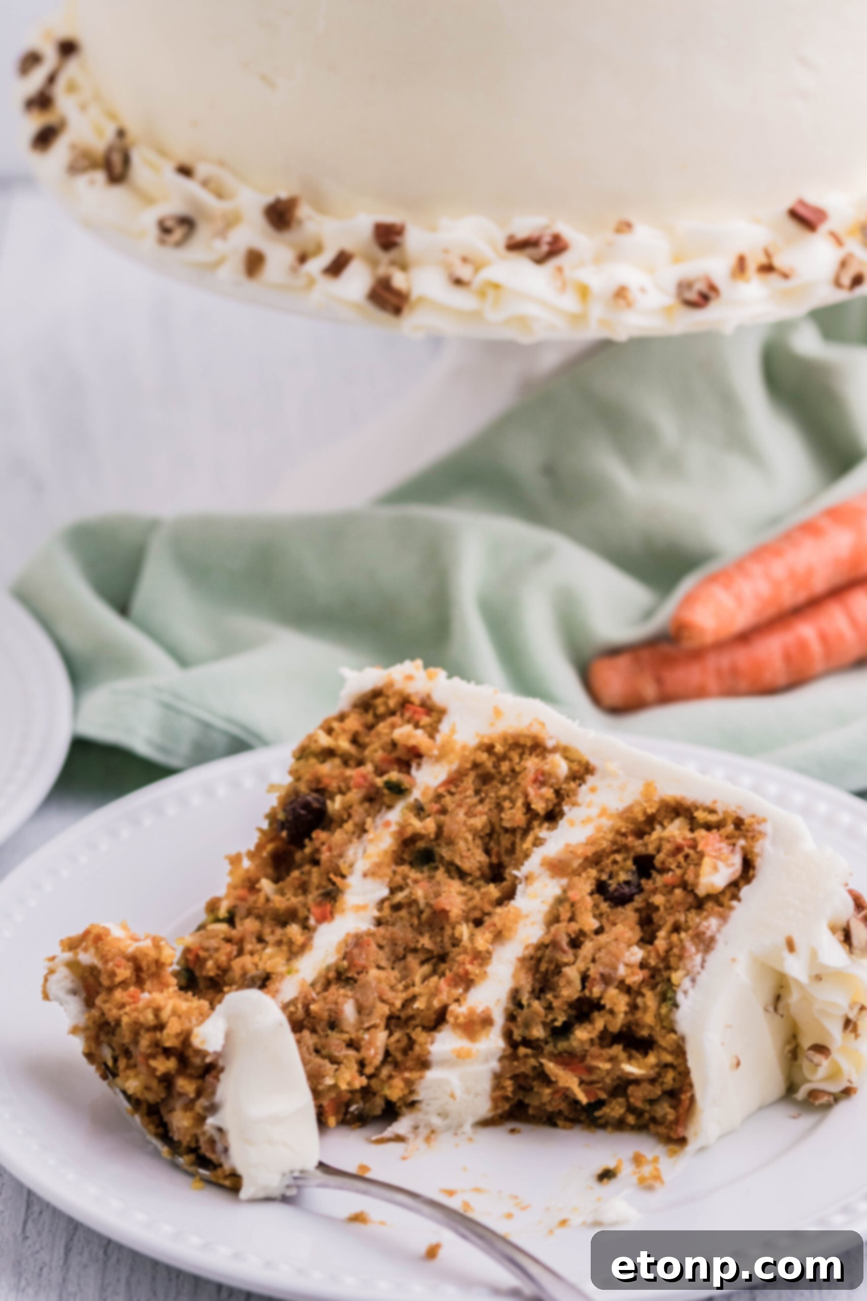 A fork holding a bite of carrot cake, hovering over a slice of cake on a white plate with a bite already taken, suggesting pure indulgence.