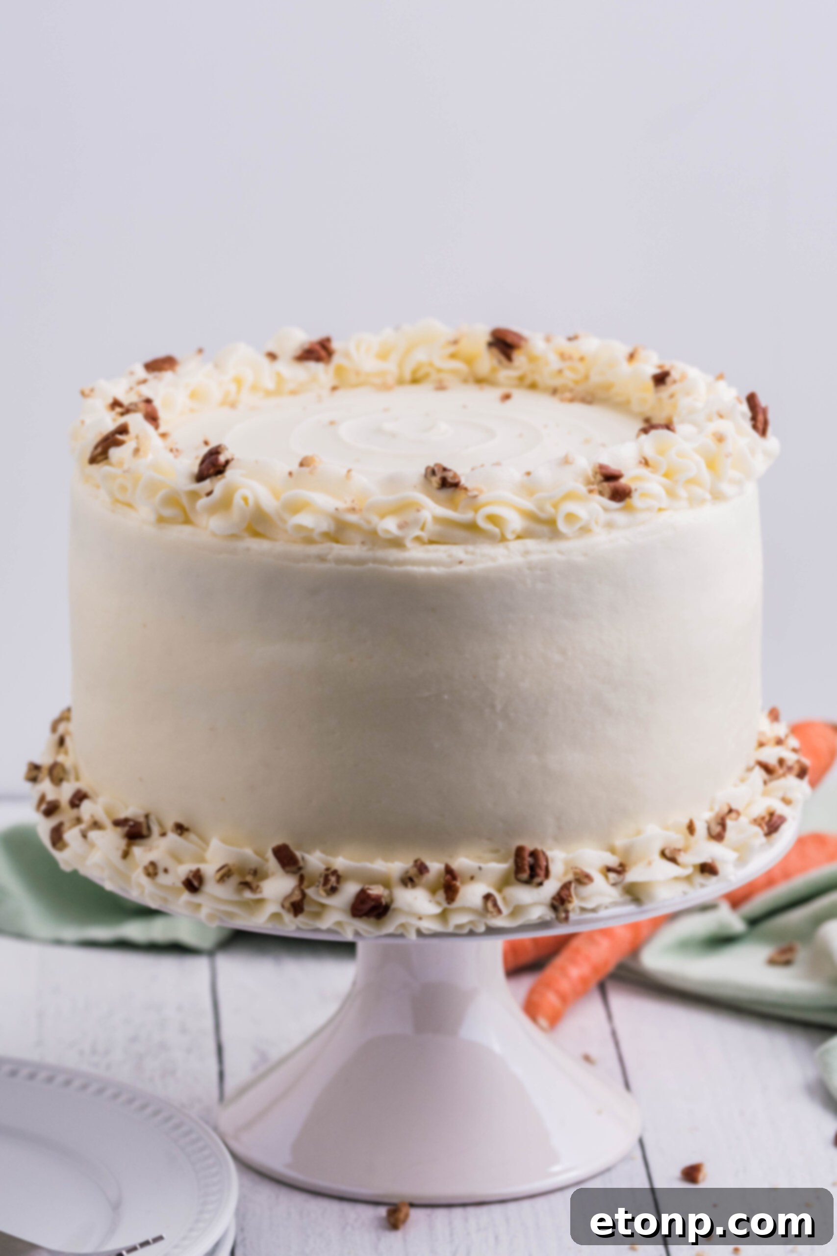 A whole, perfectly frosted homemade carrot cake sitting elegantly on a pristine white cake stand, ready to be served.