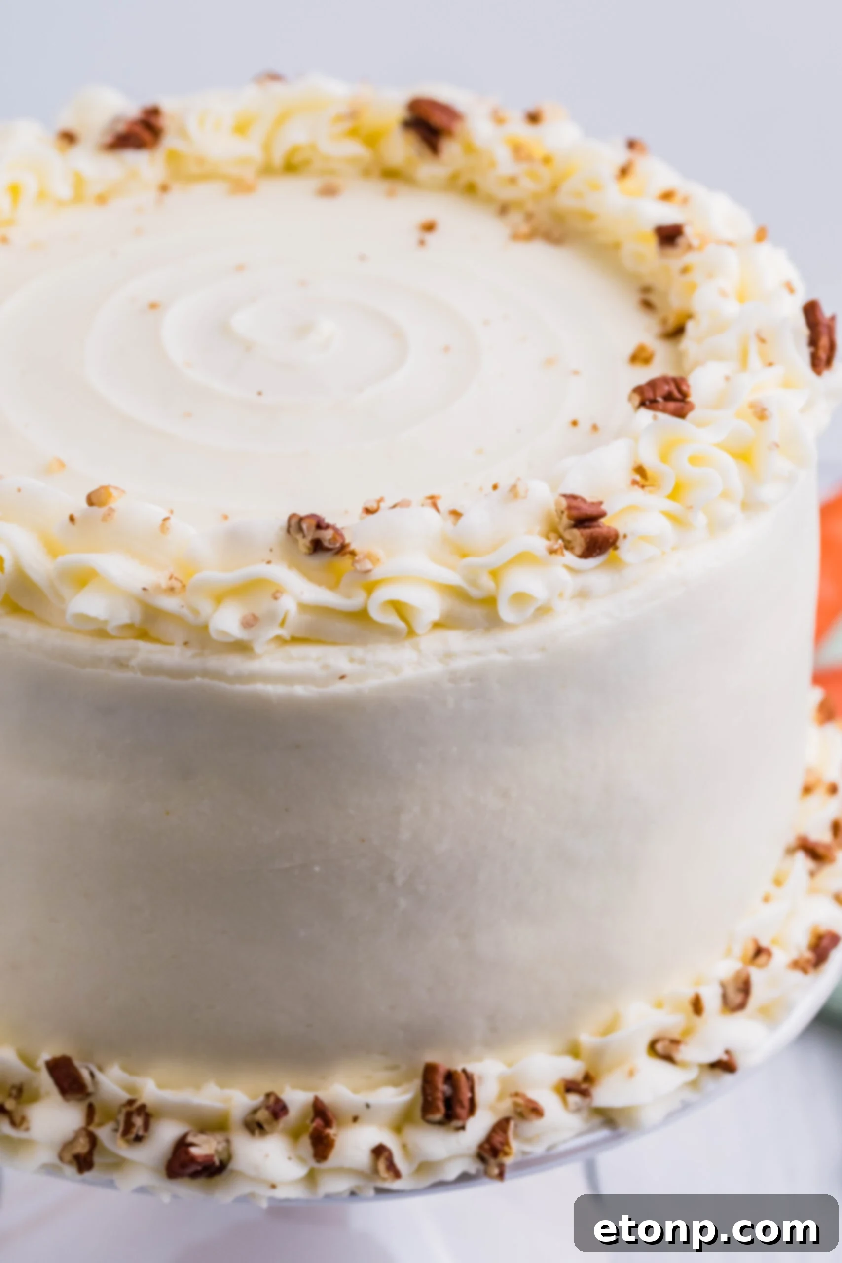 A close-up view of the top of a frosted homemade carrot cake, showcasing the smooth, creamy texture of the cream cheese frosting.