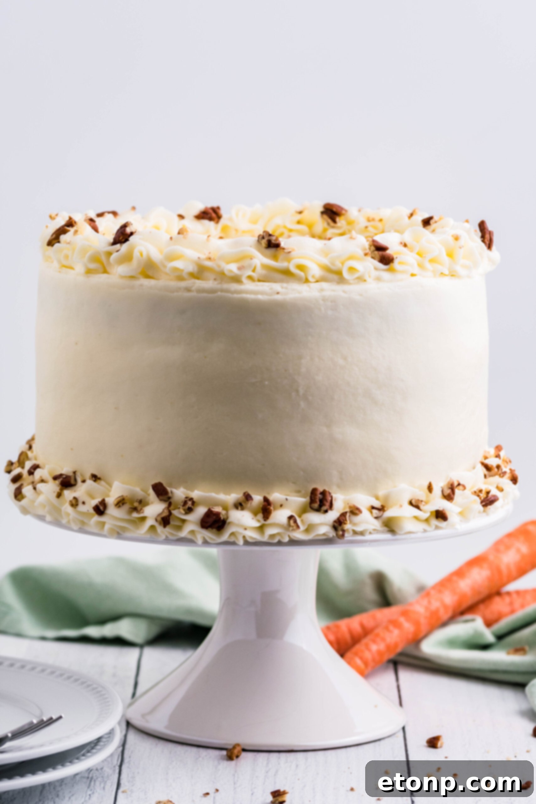A beautifully arranged carrot cake on a white cake stand, highlighting its tall layers and thick, creamy frosting, with decorative elements on top.